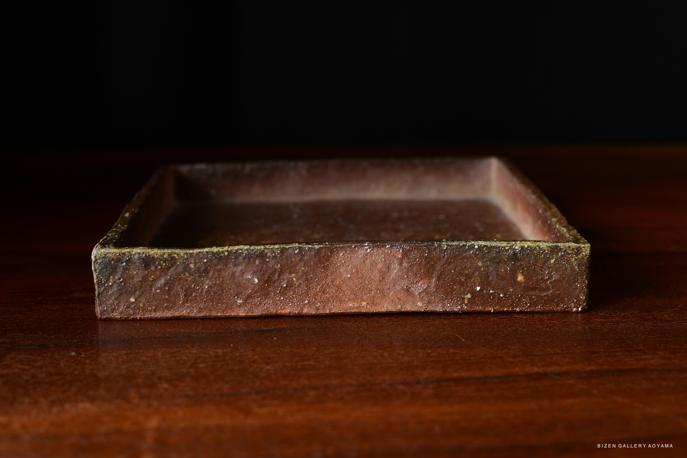 A simple square plate in a classic brown color, with a slightly textured surface, placed on a wooden table.