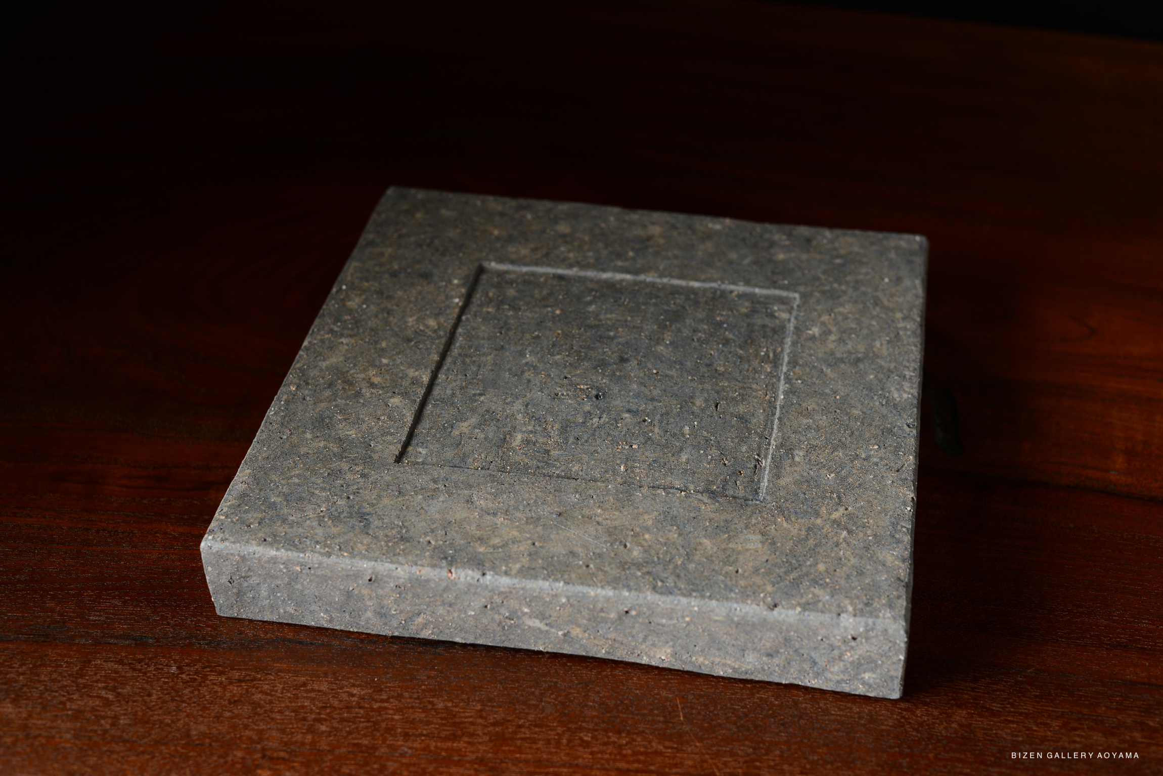 A simple and stylish square plate in a neutral tone, showcasing a subtle texture, placed against a dark wooden background.