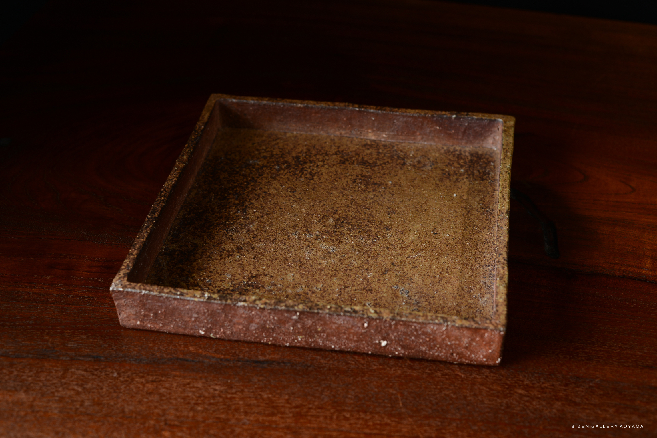 A simple square ceramic plate with a textured brown surface, placed on a wooden table.