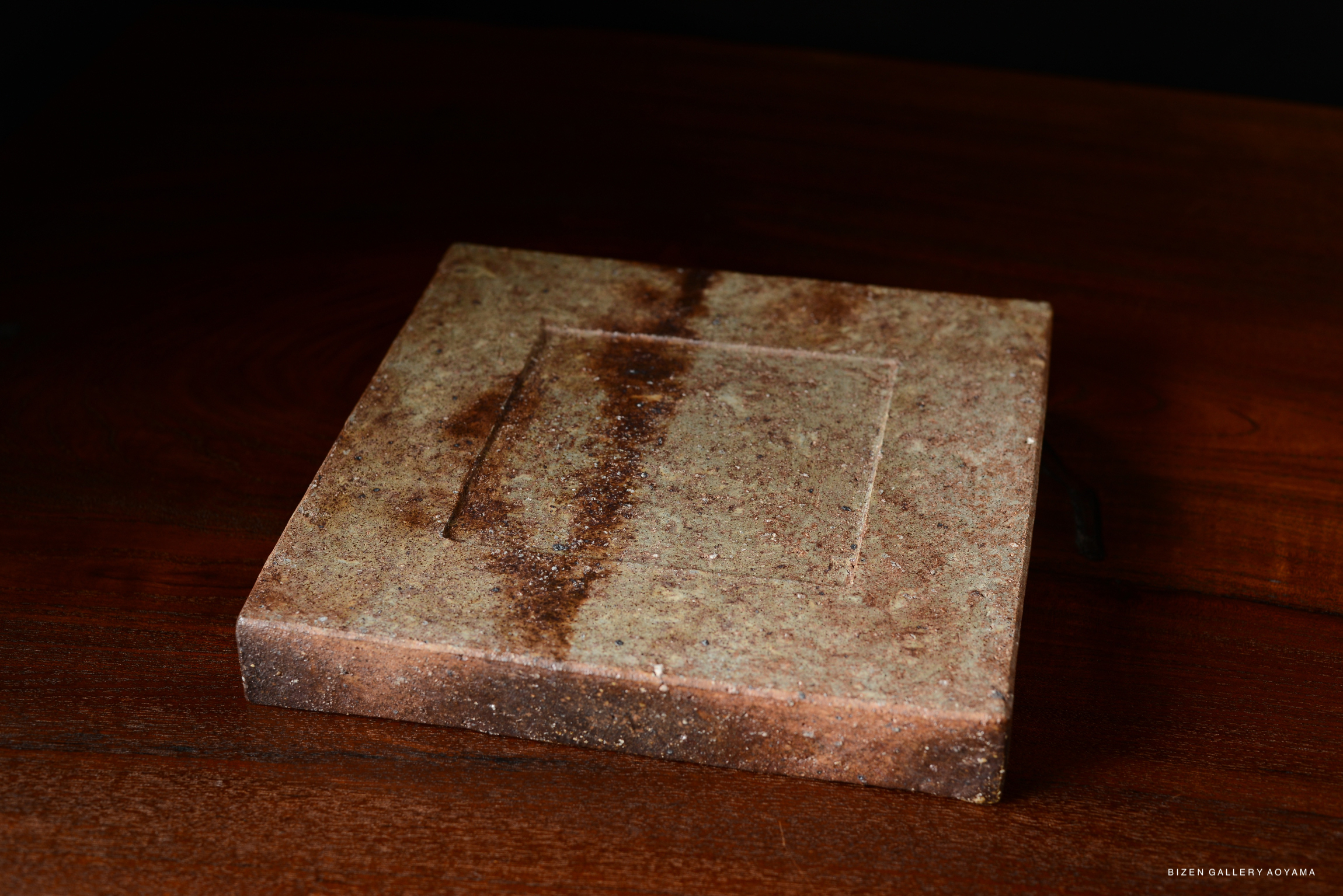 A square plate with a textured surface in earthy tones, resting on a wooden table.