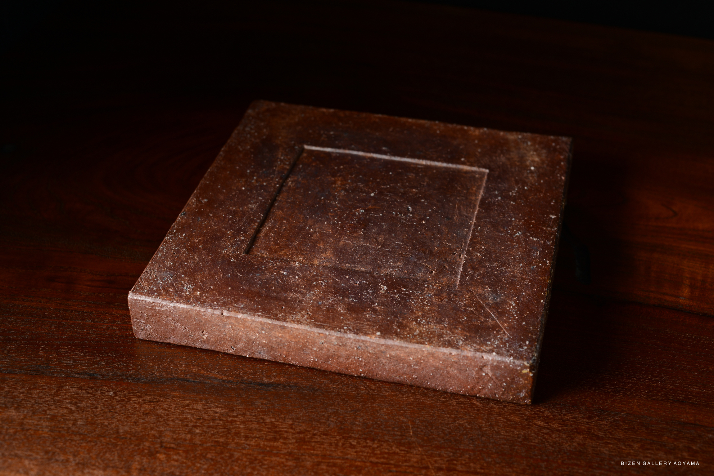 A simple and chic square plate with a textured surface, sitting on a wooden table, showcasing a brown color.