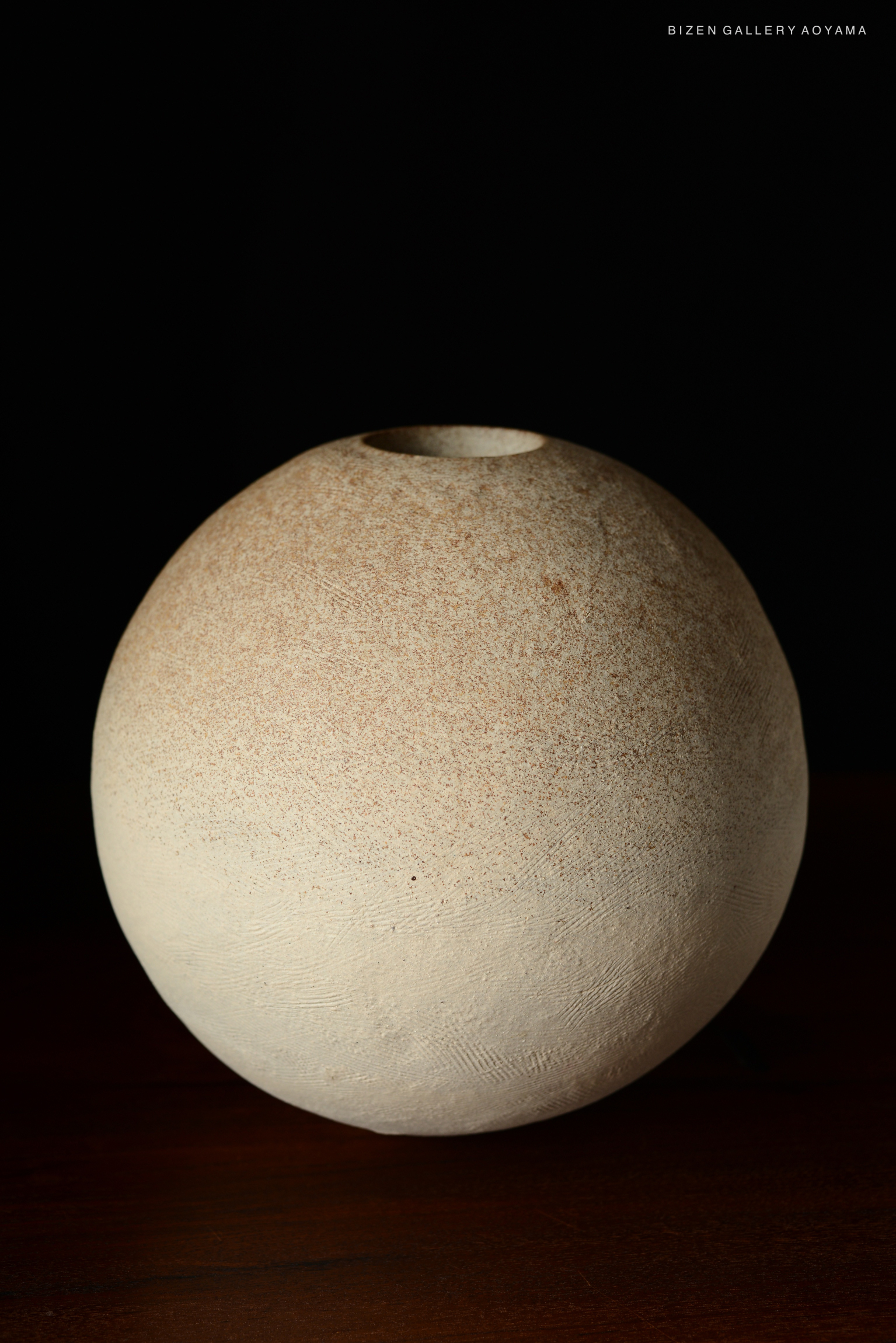 A spherical Bizen vase with a textured surface and a narrow opening on top, set against a dark background.
