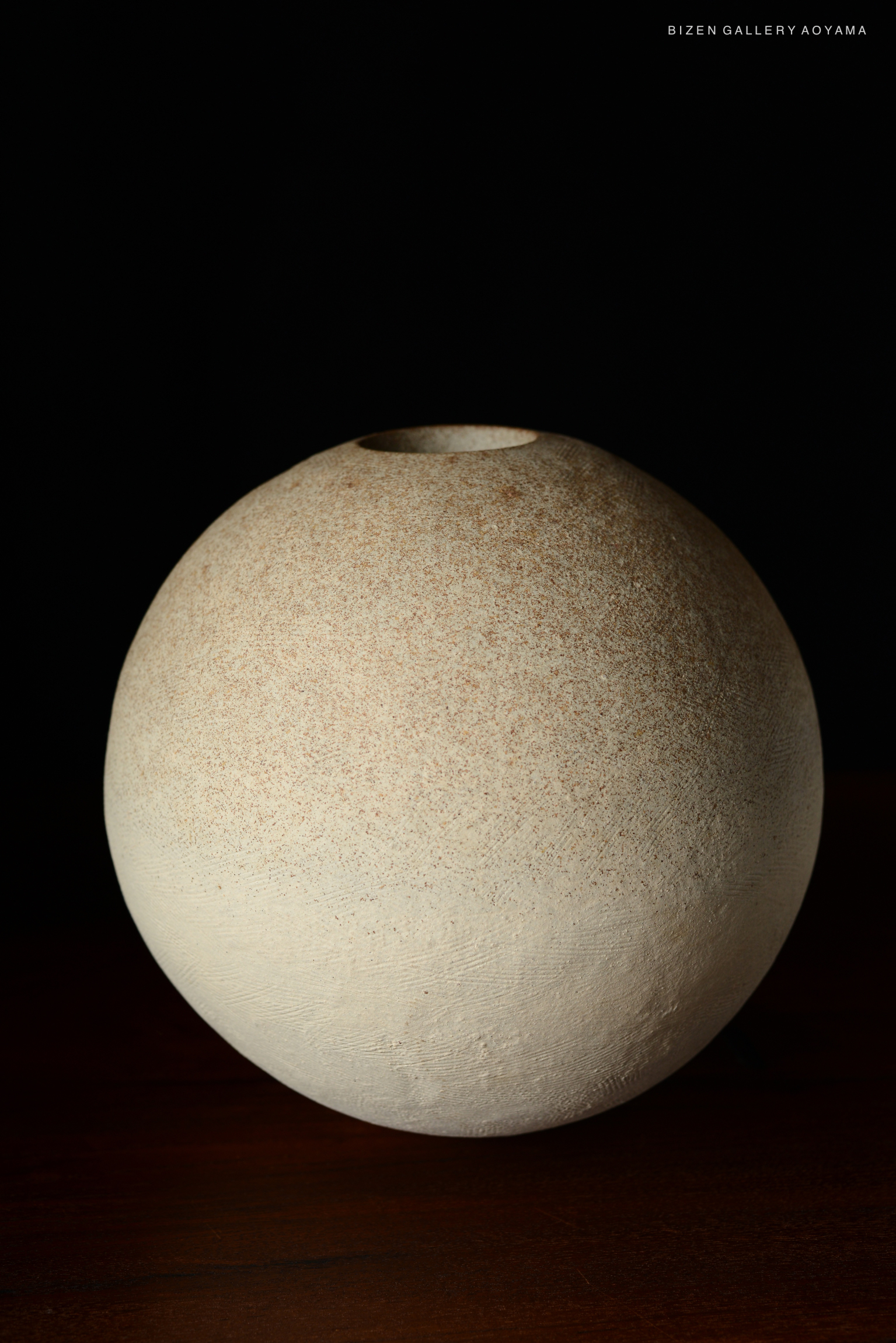A spherical Bizen pottery vase with a textured, earthy surface and a narrow opening at the top, set against a dark background.
