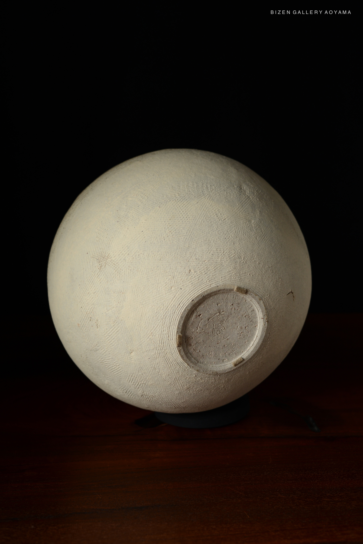 A spherical white ceramic vase with textured surface and a flat base, placed on a dark wooden table.