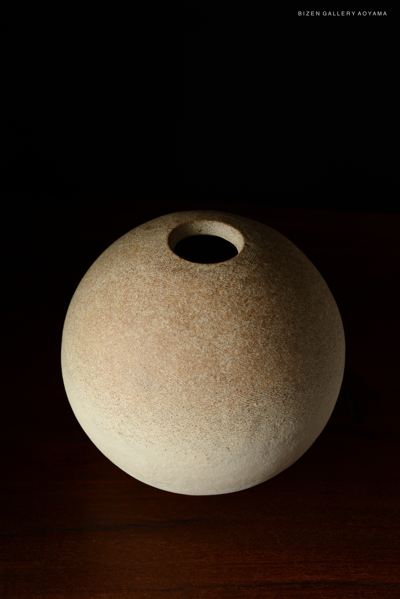 A round, lightly textured Bizen pottery vase with a small opening on top, displayed against a dark background.