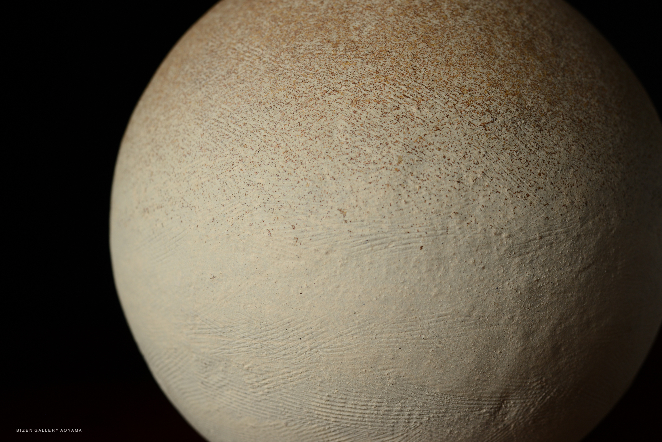 Close-up of a beige spherical ceramic piece with a textured surface against a dark background, showcasing natural variations and subtle imperfections.