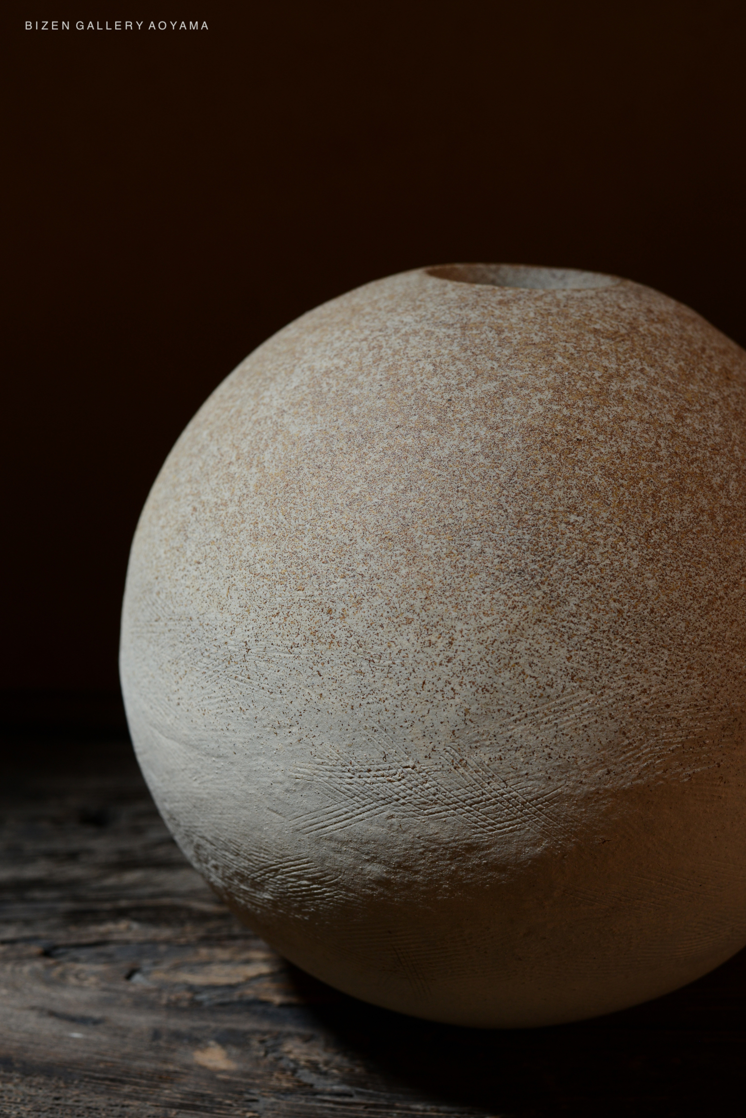 Close-up of a textured, round Bizen pottery vase, showcasing a natural earthy color against a dark background.