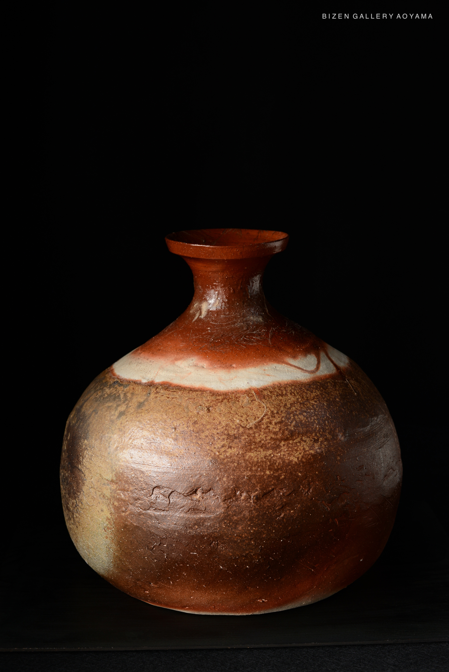 A Bizen ware Tokkuri, featuring a rounded body and narrow neck, displaying rich earthy tones and textures against a dark background.