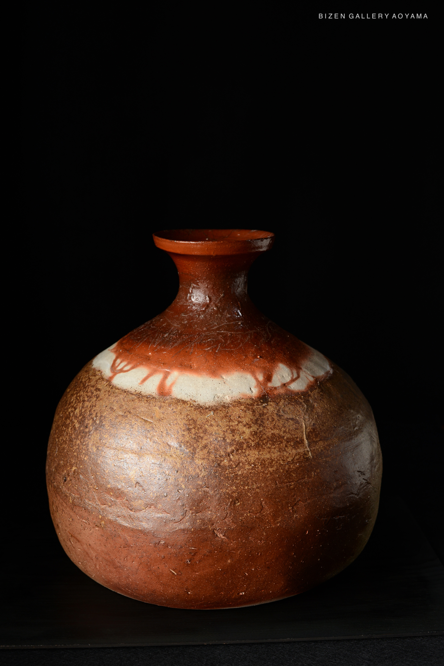 A traditional Bizen pottery Tokkuri with a round body and a narrow neck, showcasing earthy tones and a distinctive glaze, set against a black background.