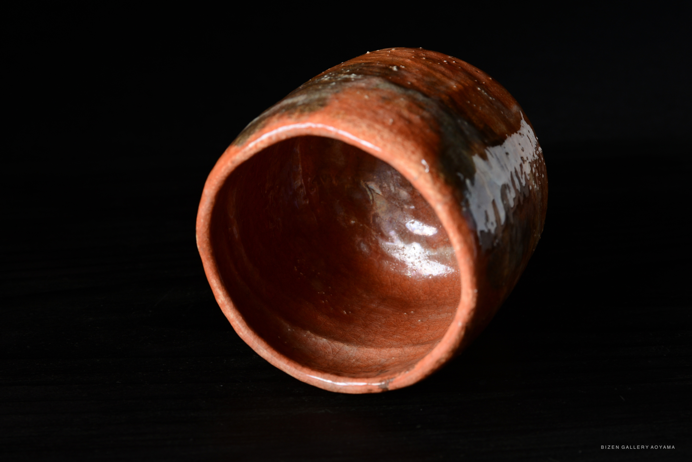 A close-up view of a red ceramic tea bowl, showcasing its interior and outer texture, placed on a dark surface.