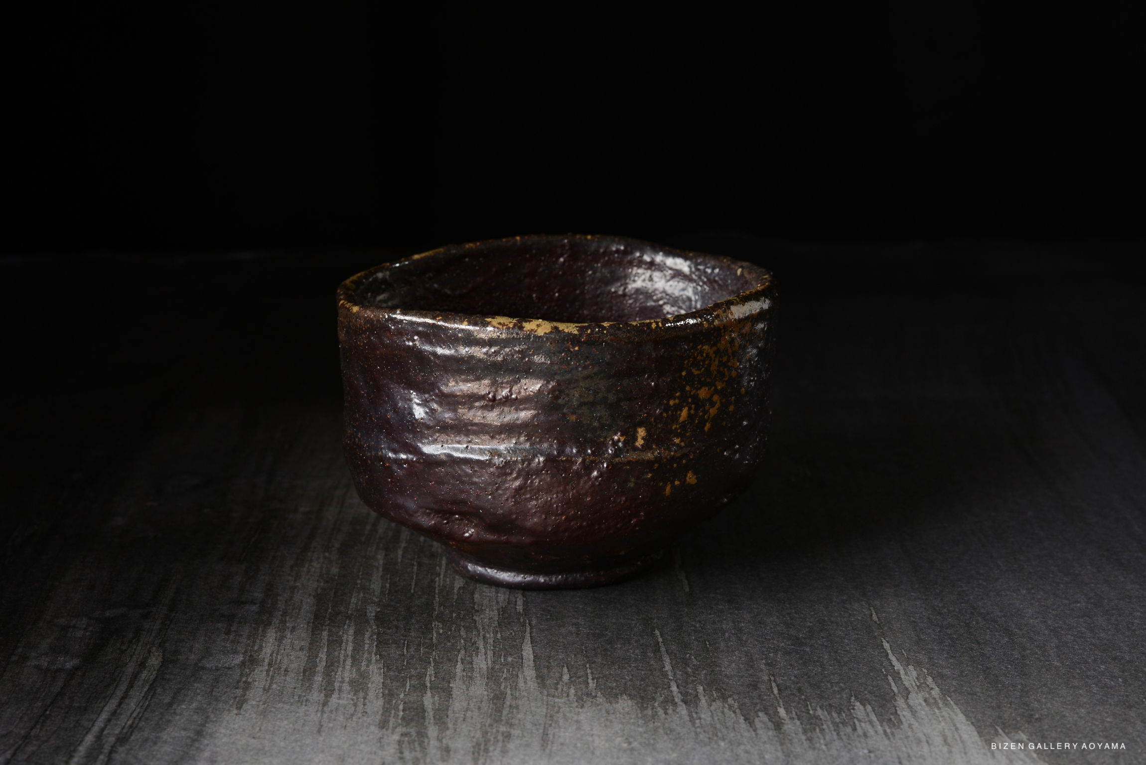 A rustic ceramic bowl with a textured surface and a dark finish, set against a dark background.