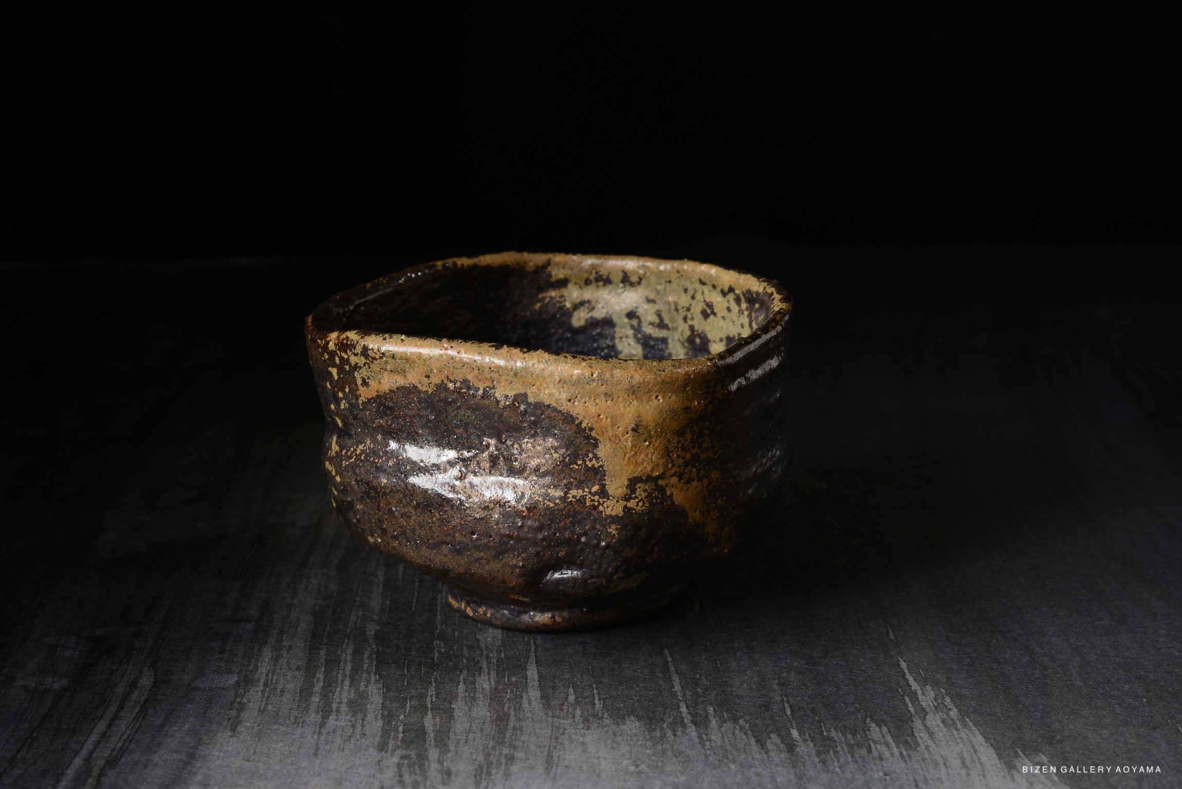 A textured, rustic ceramic bowl with a dark exterior and a lighter interior, placed on a dark surface with subtle lighting.
