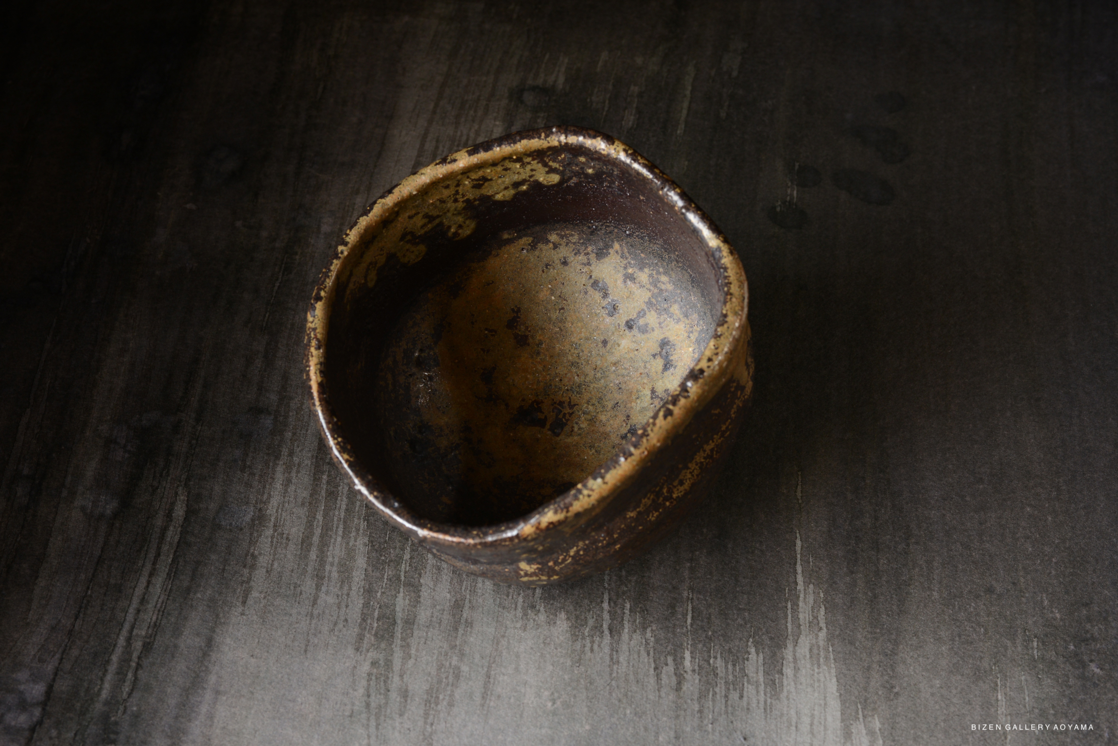 A close-up view of a rustic, round ceramic bowl with a textured surface, set against a dark wooden background.