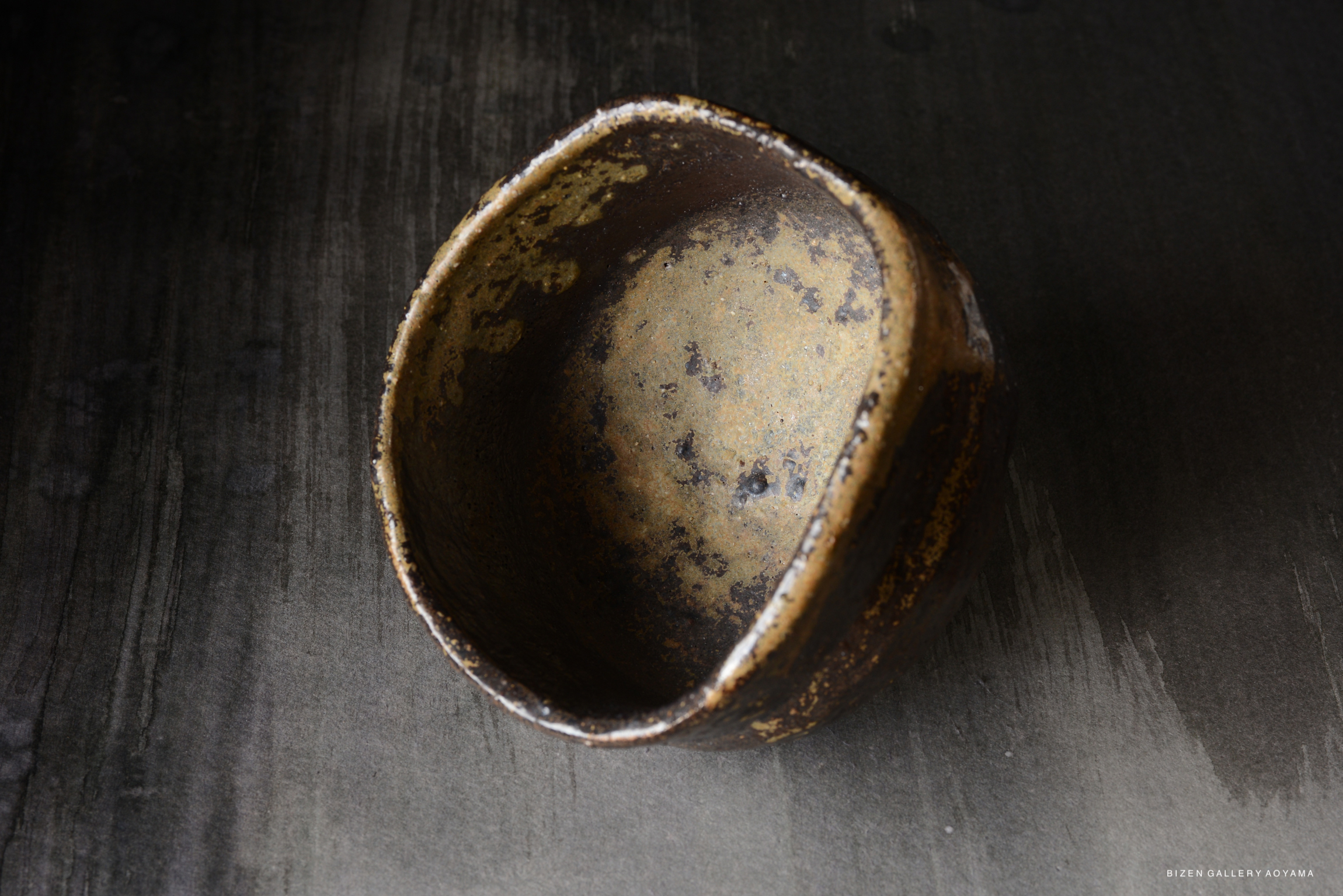 A close-up view of a rustic ceramic bowl with a textured surface, displaying earthy tones, set against a dark background.