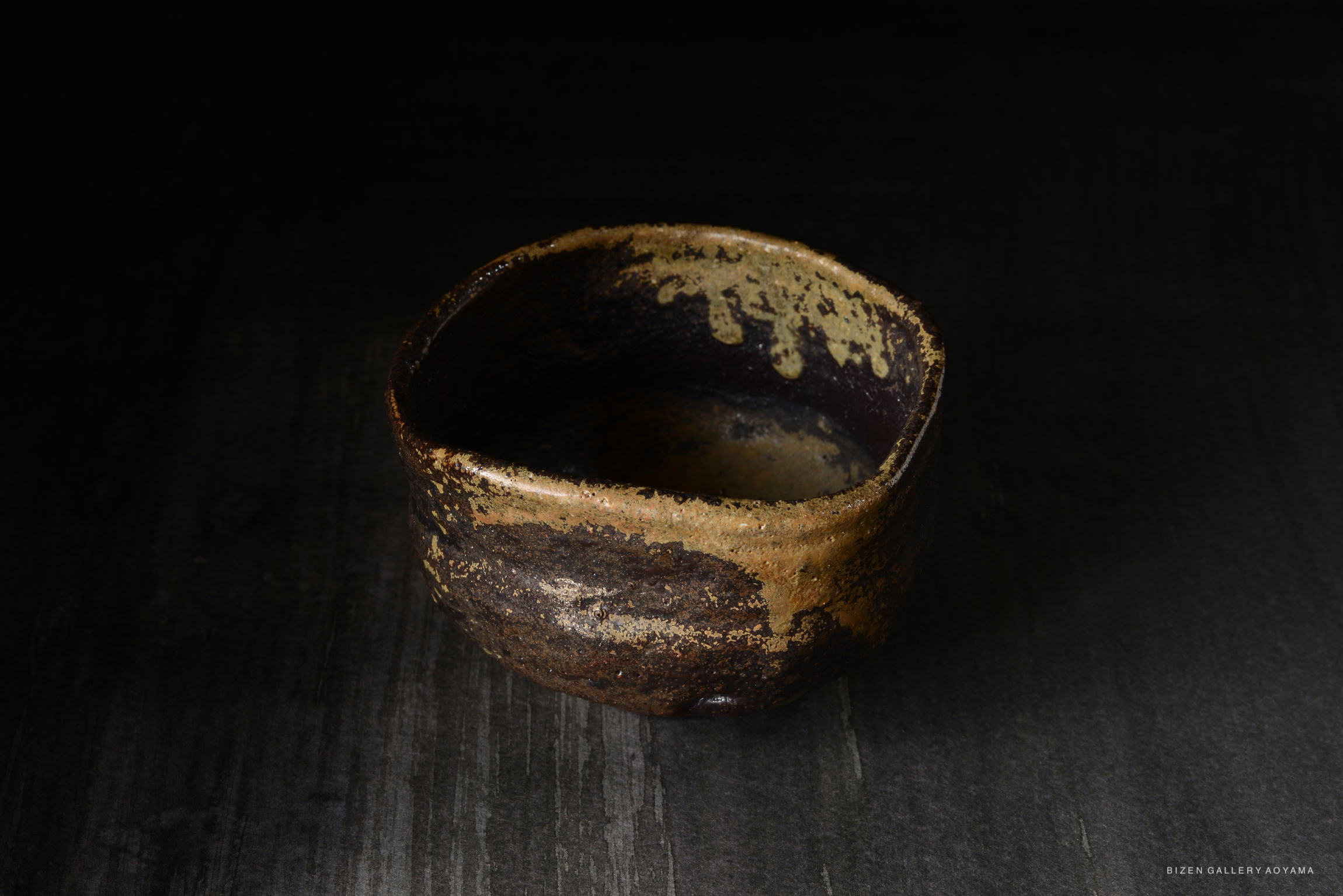 A rustic ceramic bowl featuring a textured surface with earthy tones of brown and beige, set against a dark background.