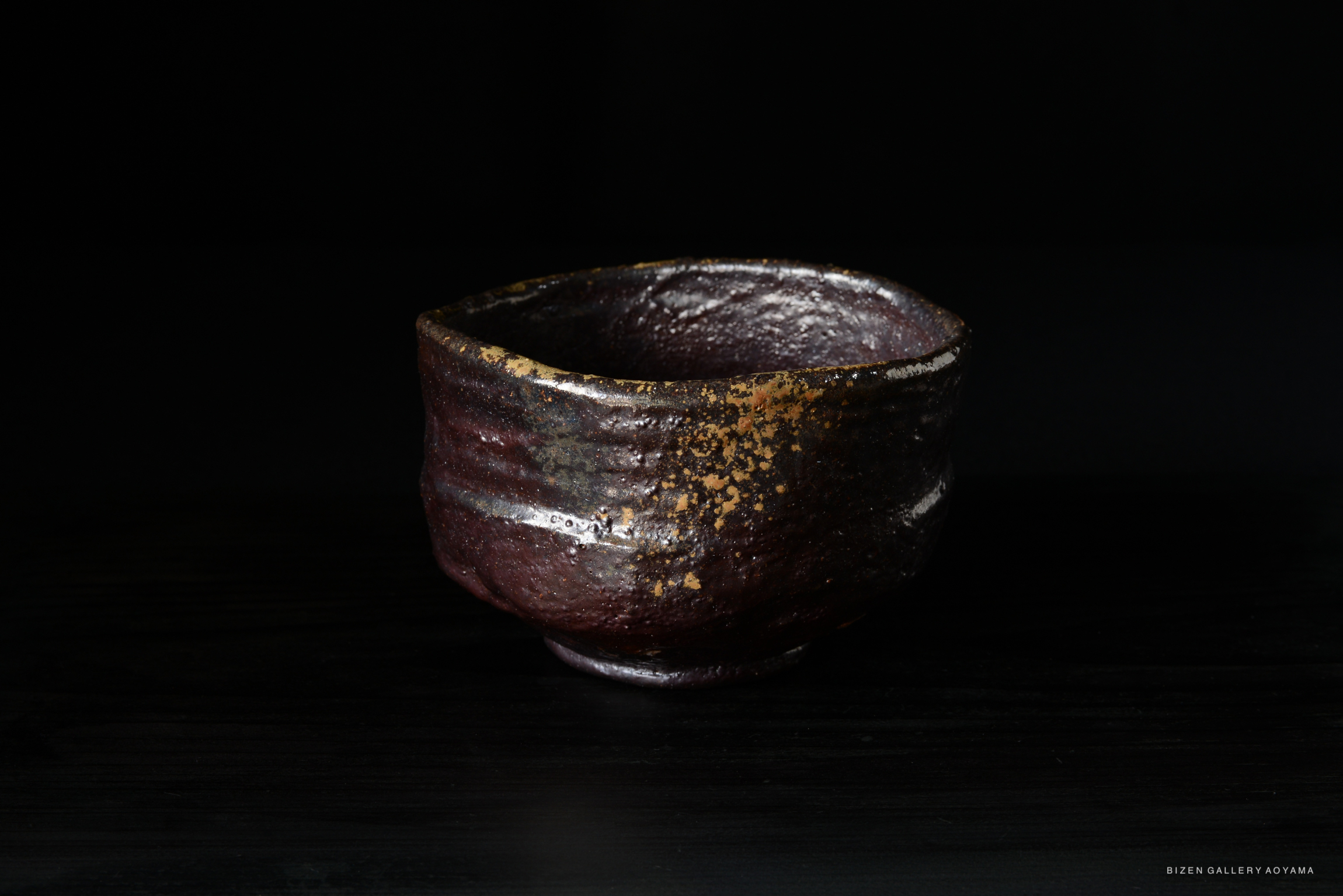 A dark, rustic ceramic bowl with a textured surface and speckles of gold, placed on a black background.