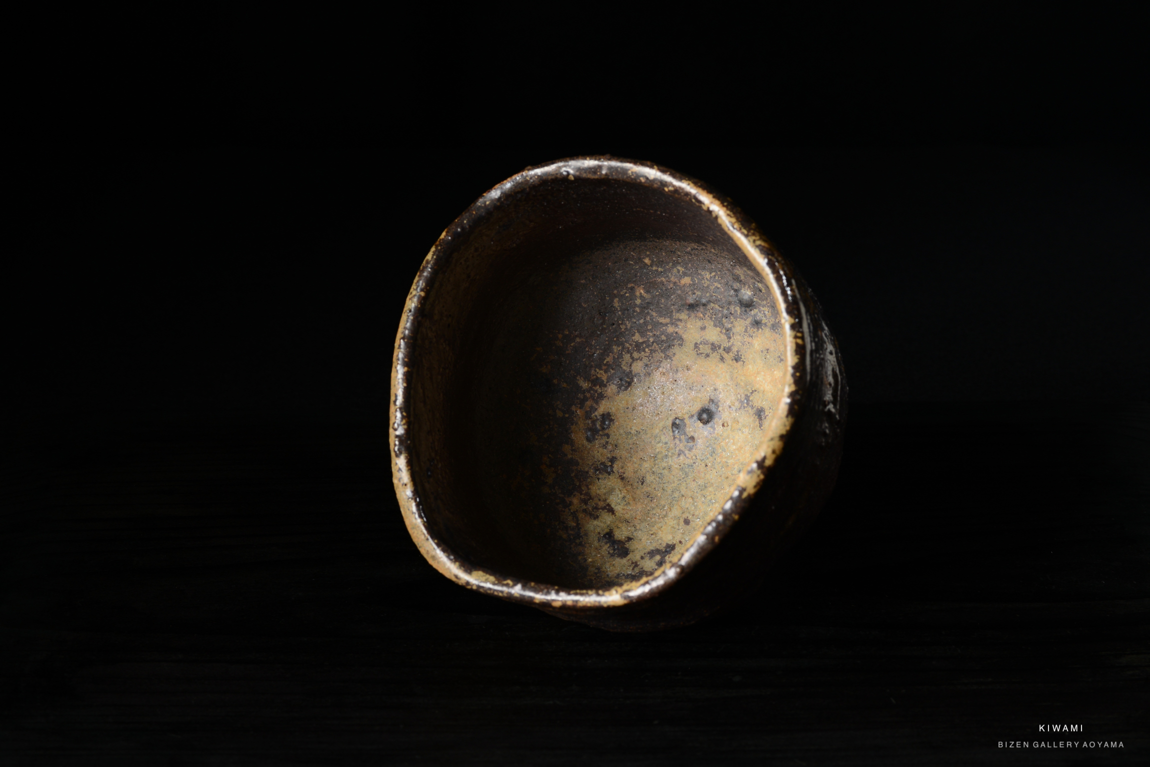 A close-up view of a rustic ceramic bowl with a textured surface and natural coloring, set against a dark background.