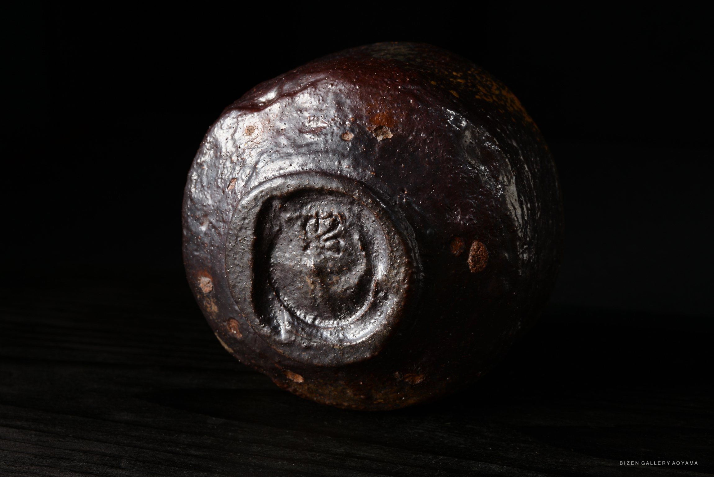 A close-up of a round, dark ceramic object with a circular stamp or indentation on its surface, set against a black background.