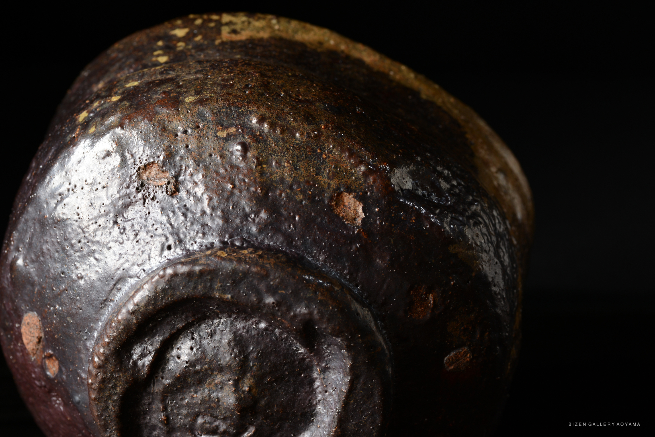 Close-up of a dark, textured ceramic piece with a rich, glossy surface and subtle imperfections, set against a dark background.