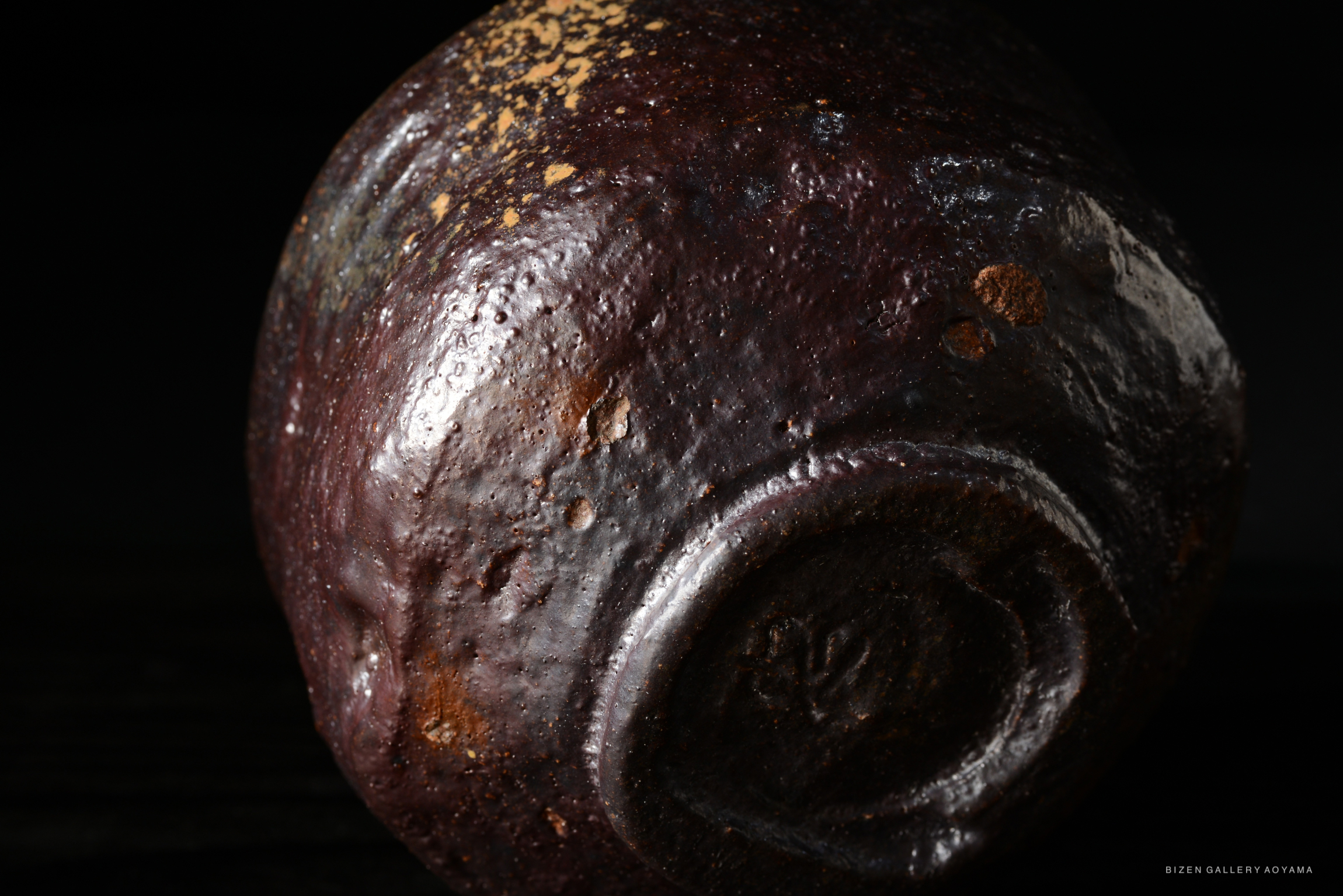 Close-up of a round, textured ceramic piece with a dark, glossy surface, revealing subtle color variations and imperfections.