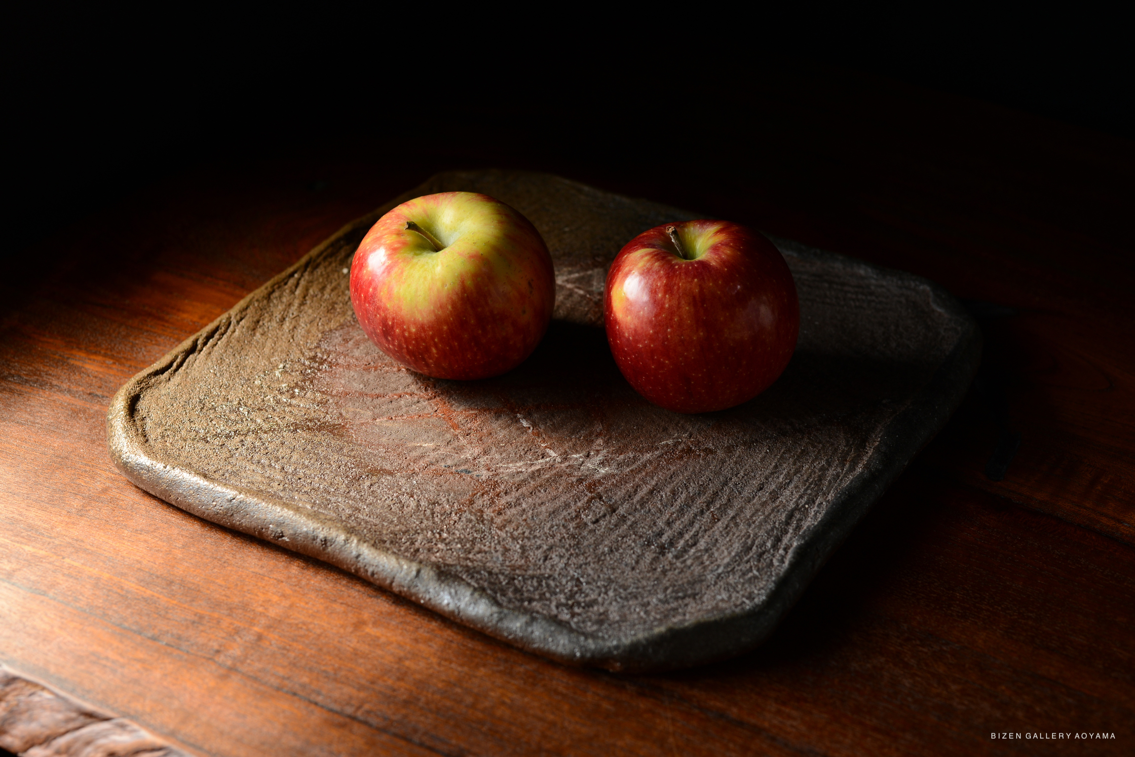 Two red apples resting on a rustic, textured plate against a dark background.