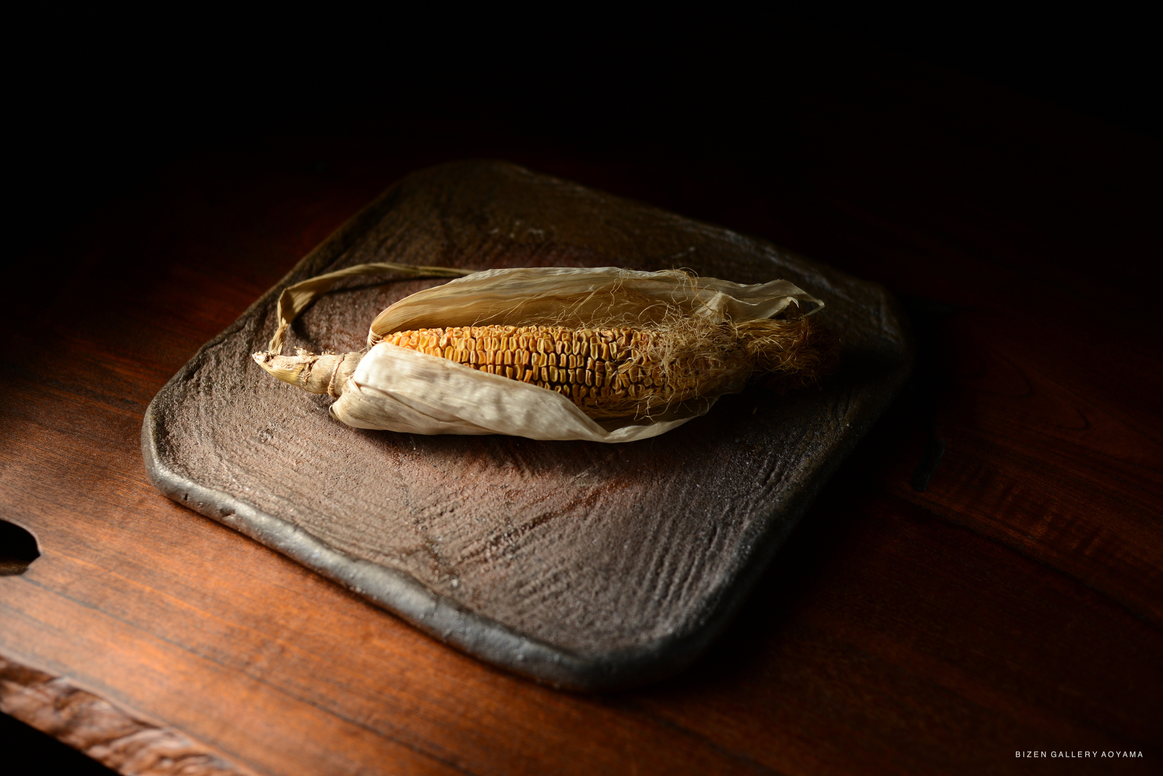 A close-up of dried corn on a textured ceramic plate, resting on a wooden surface.
