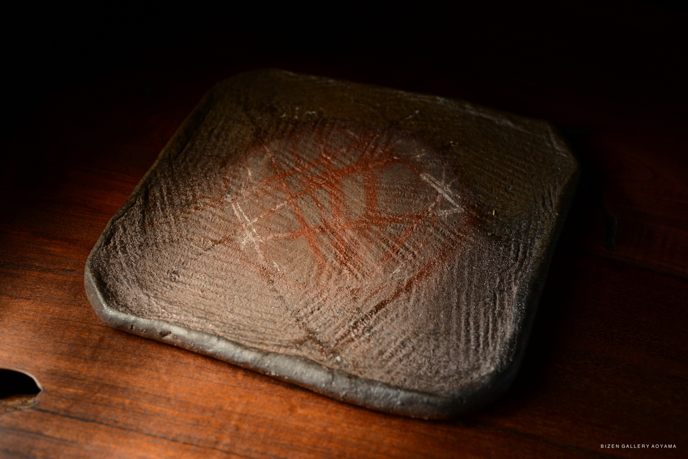 A close-up view of a decorative square ceramic plate with a textured surface, resembling a garden stone, set against a dark background.