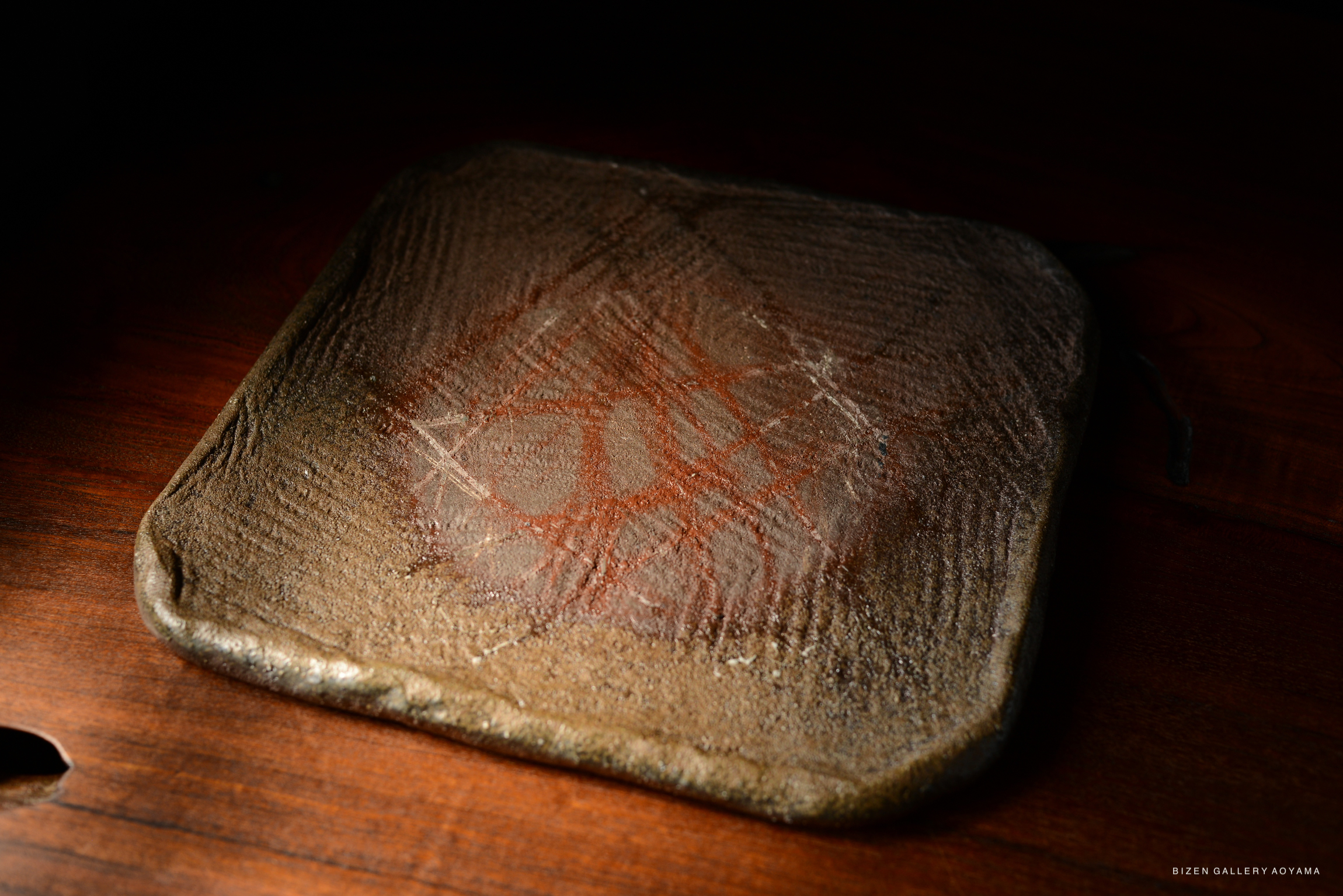 Close-up of a textured ceramic piece with abstract markings, placed on a wooden surface.