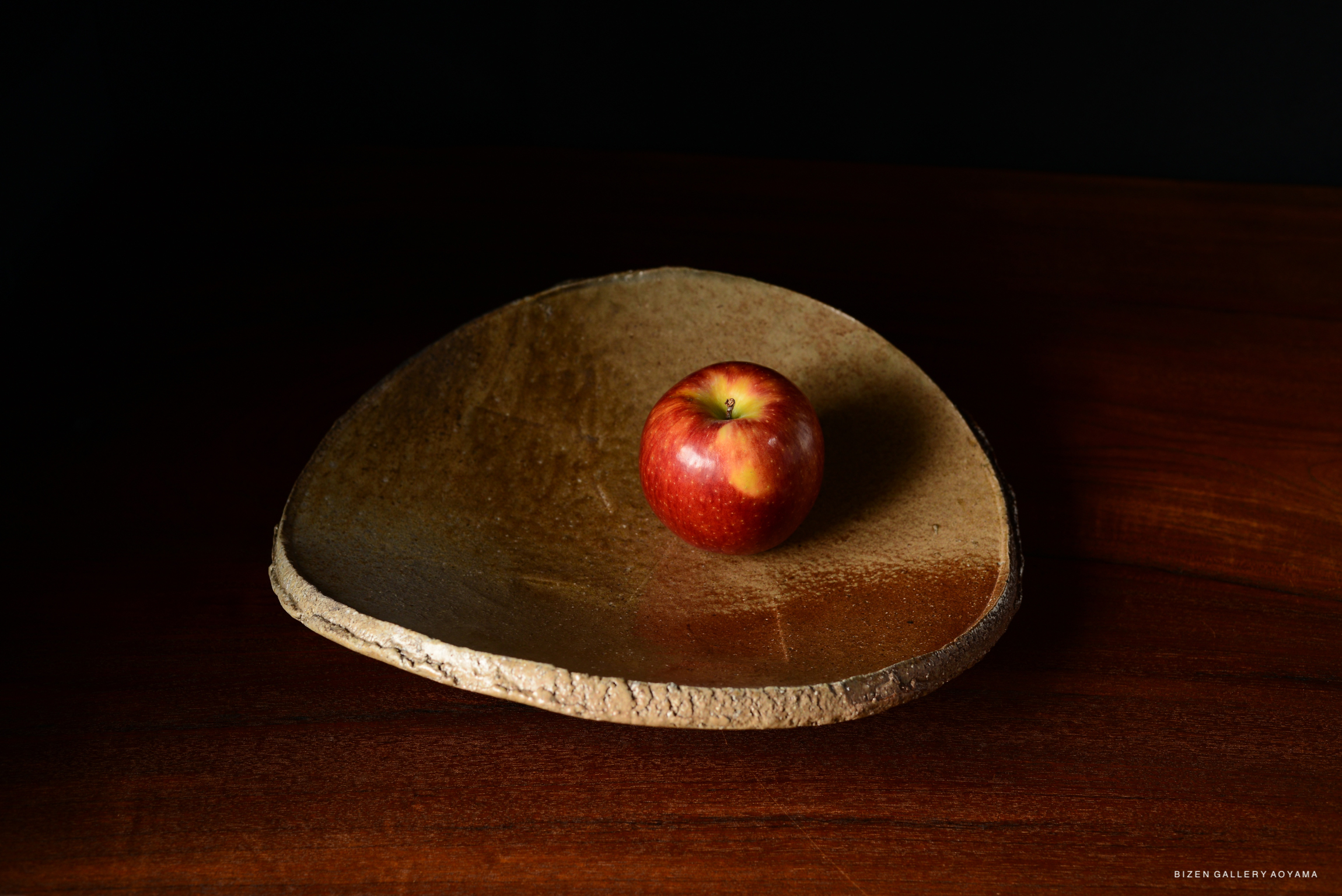 A red apple placed on a uniquely shaped, textured ceramic dish on a wooden surface.