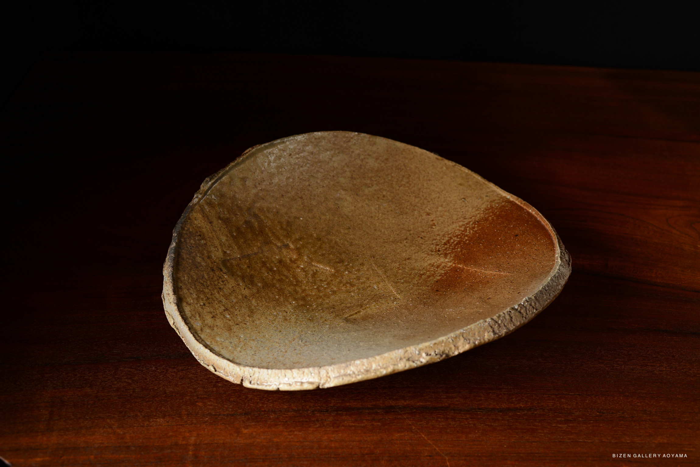 A close-up view of a rustic, curved ceramic plate with a natural glaze, placed on a wooden surface.