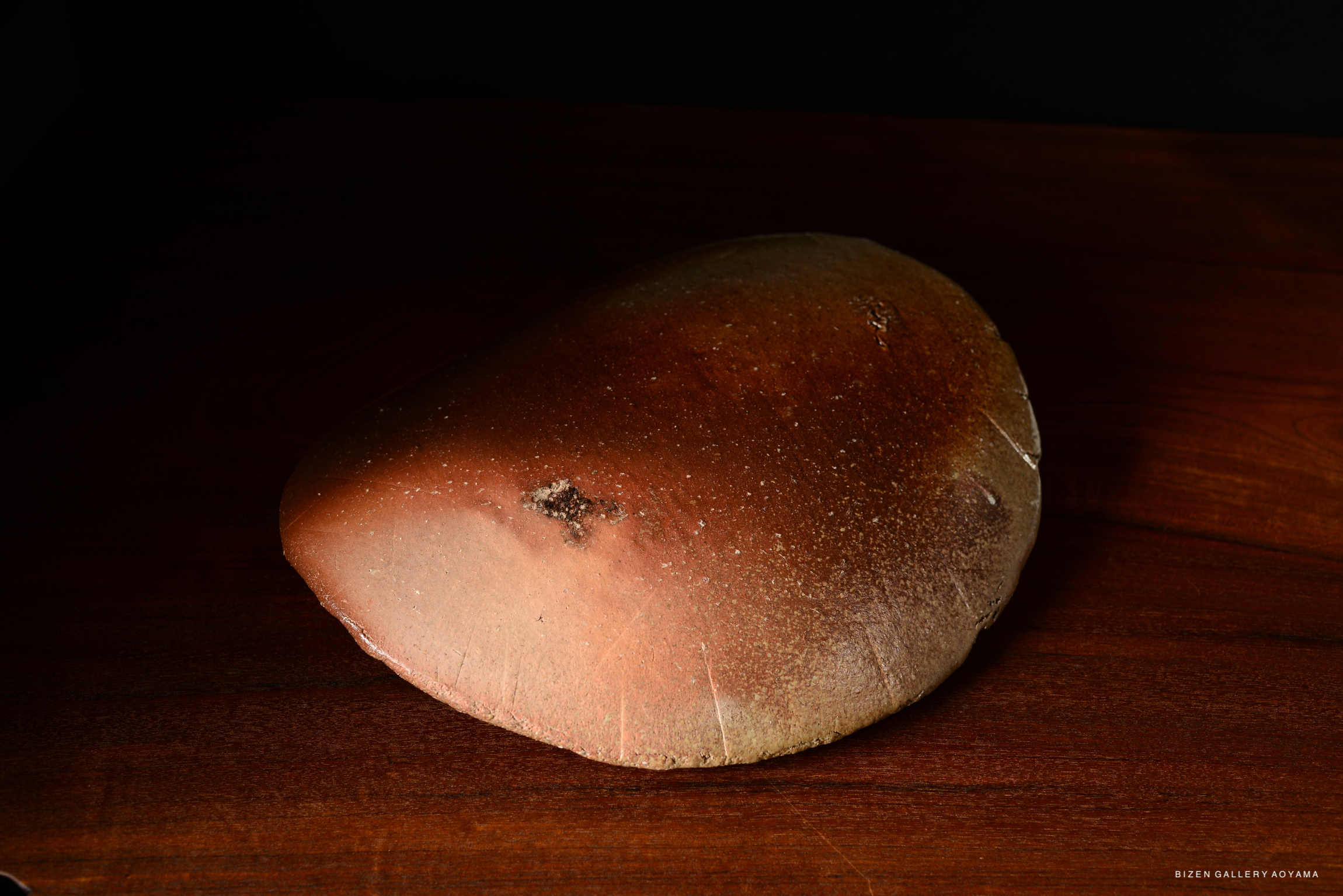 A brown, smooth ceramic object with a rounded shape, resting on a wooden surface.