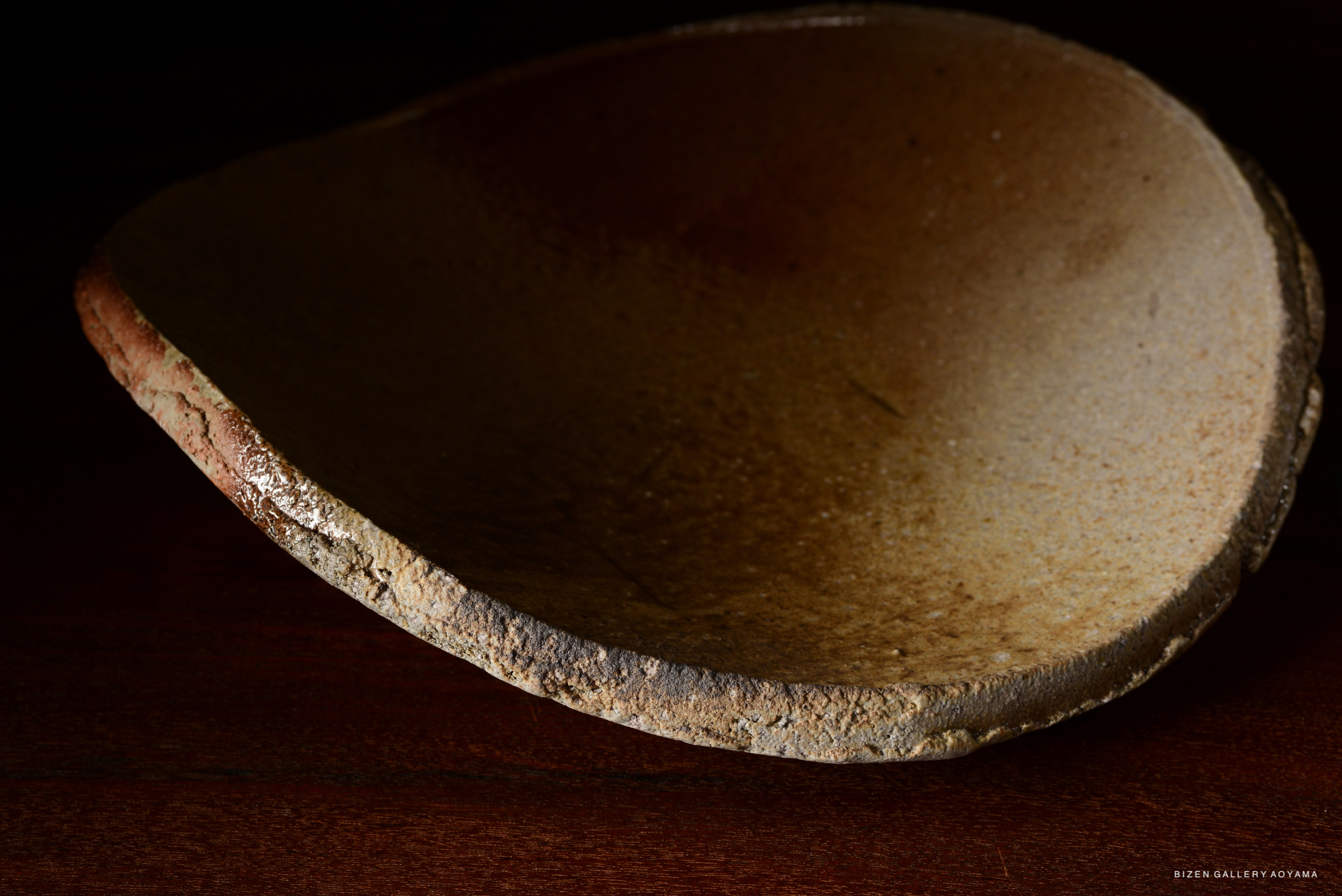 Close-up of a textured, handcrafted ceramic bowl with a natural finish, resting on a wooden surface.