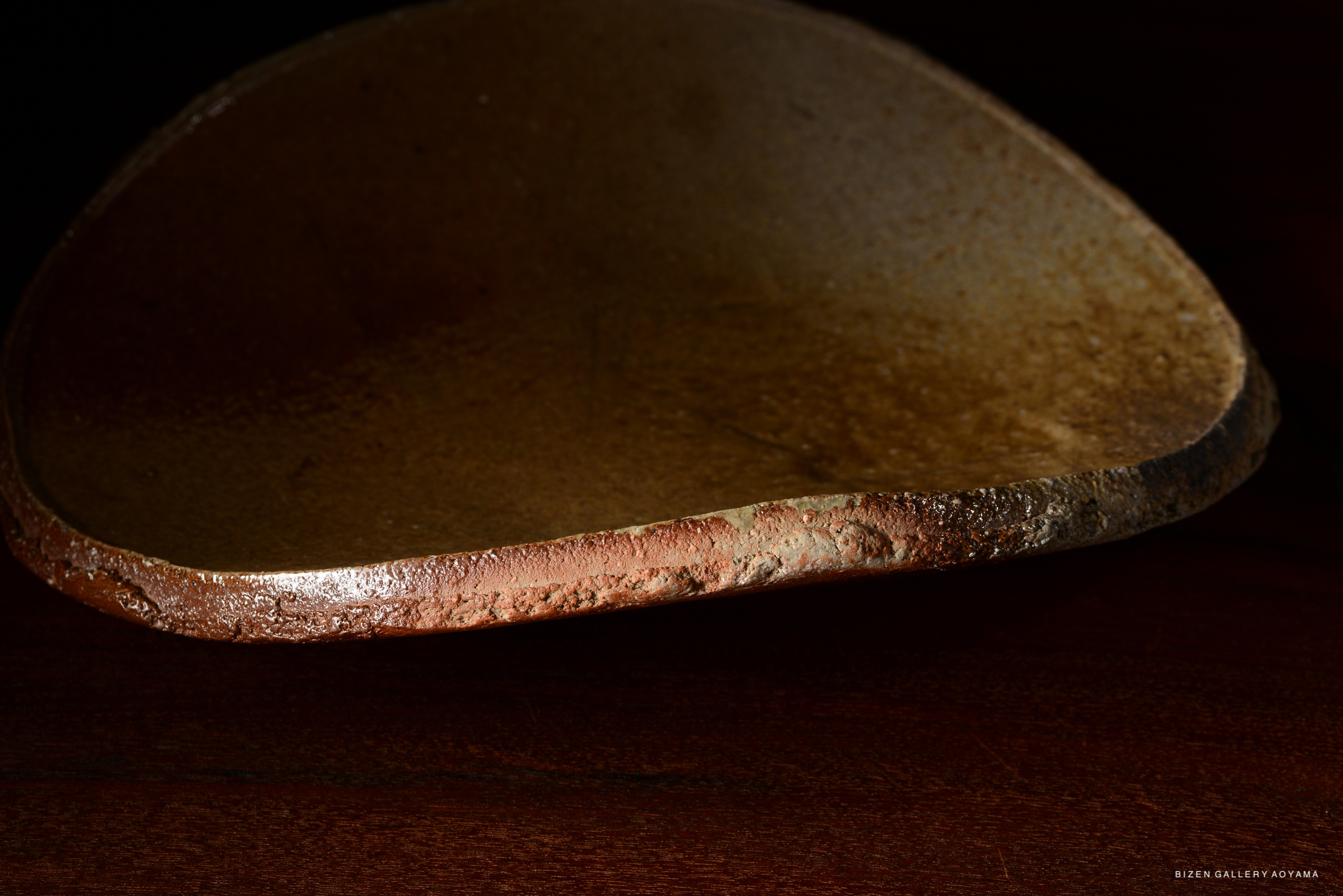 Close-up view of a textured ceramic dish with a smooth, curved edge, resting on a wooden surface.