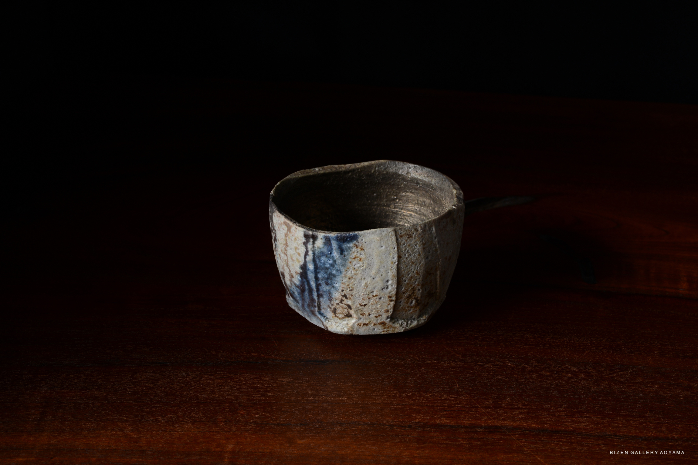 A close-up of a rustic ceramic cup with a textured surface and subtle blue streaks, placed on a dark wooden table.