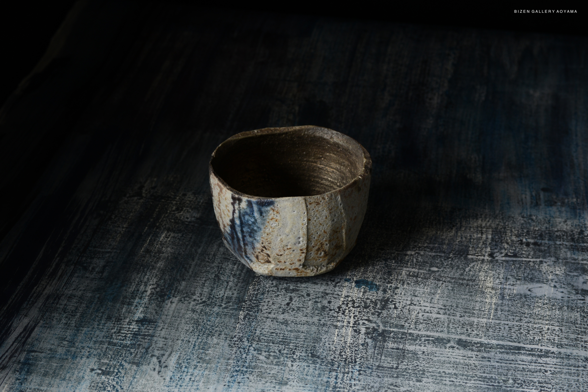A handcrafted ceramic bowl with a textured surface and muted earthy colors, set against a dark, abstract background.