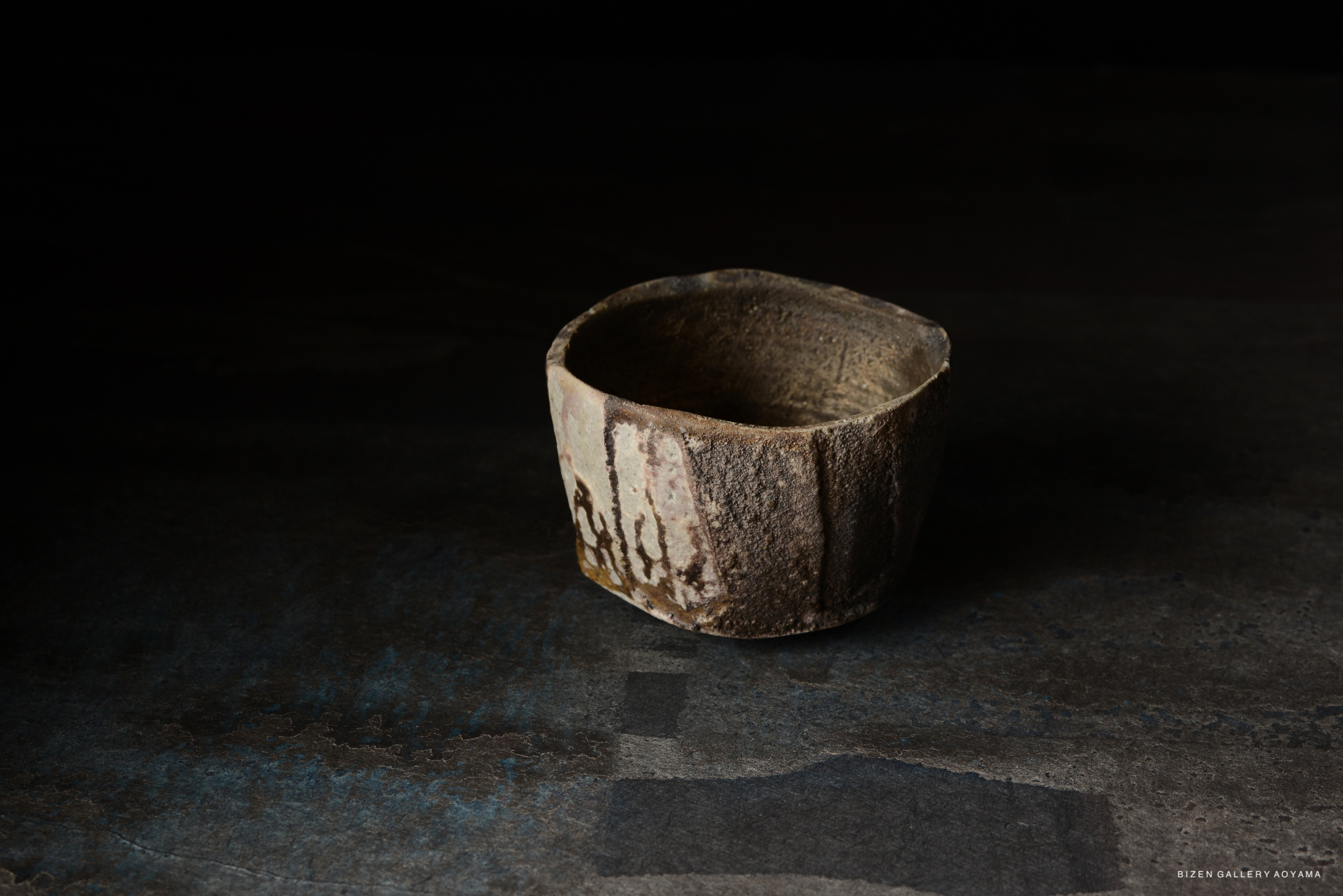 A rustic, handmade ceramic bowl placed on a textured dark surface, showcasing earthy tones and a natural finish.