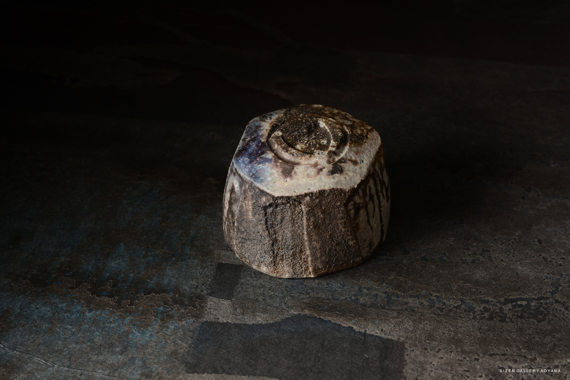 A unique ceramic piece with earthy tones and a textured surface, displayed in low light.