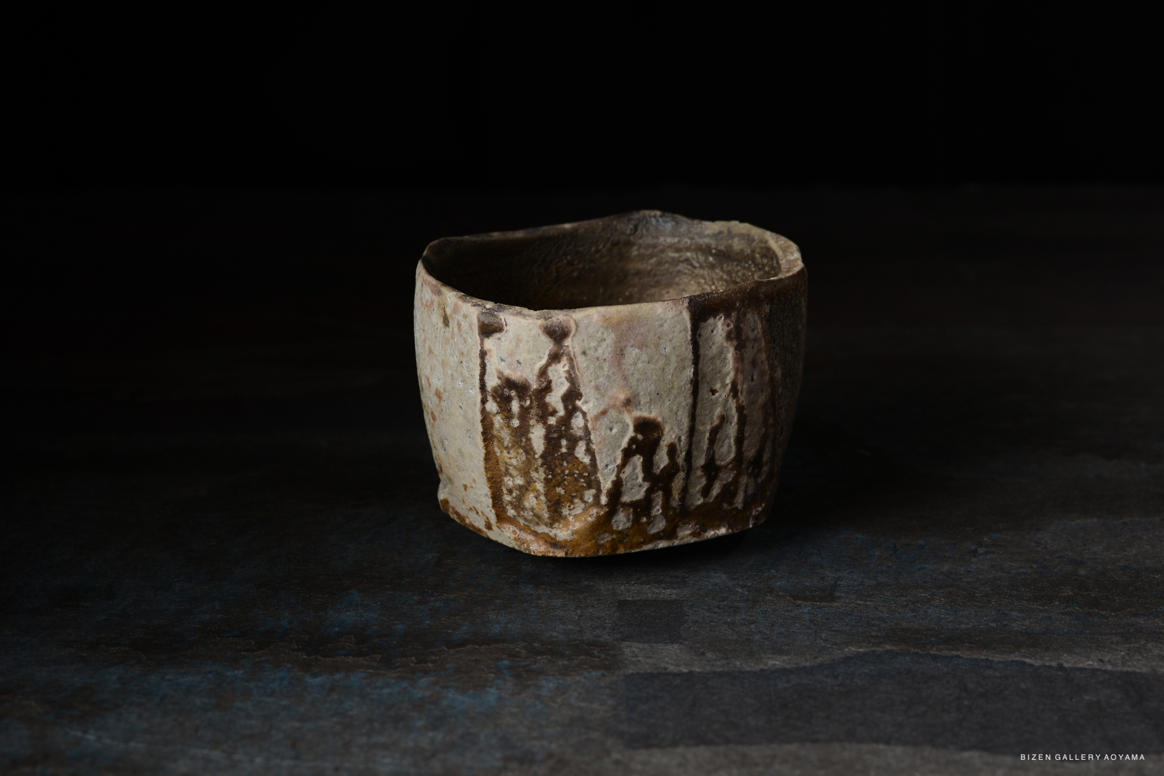 A rustic ceramic cup with a textured surface and earthy tones, placed on a dark background.