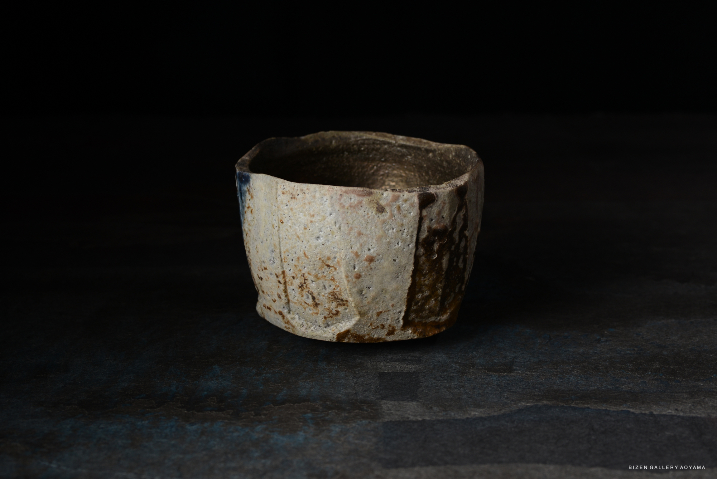 A close-up of a rustic ceramic bowl with uneven edges and textured surface, displaying natural earthy colors against a dark background.