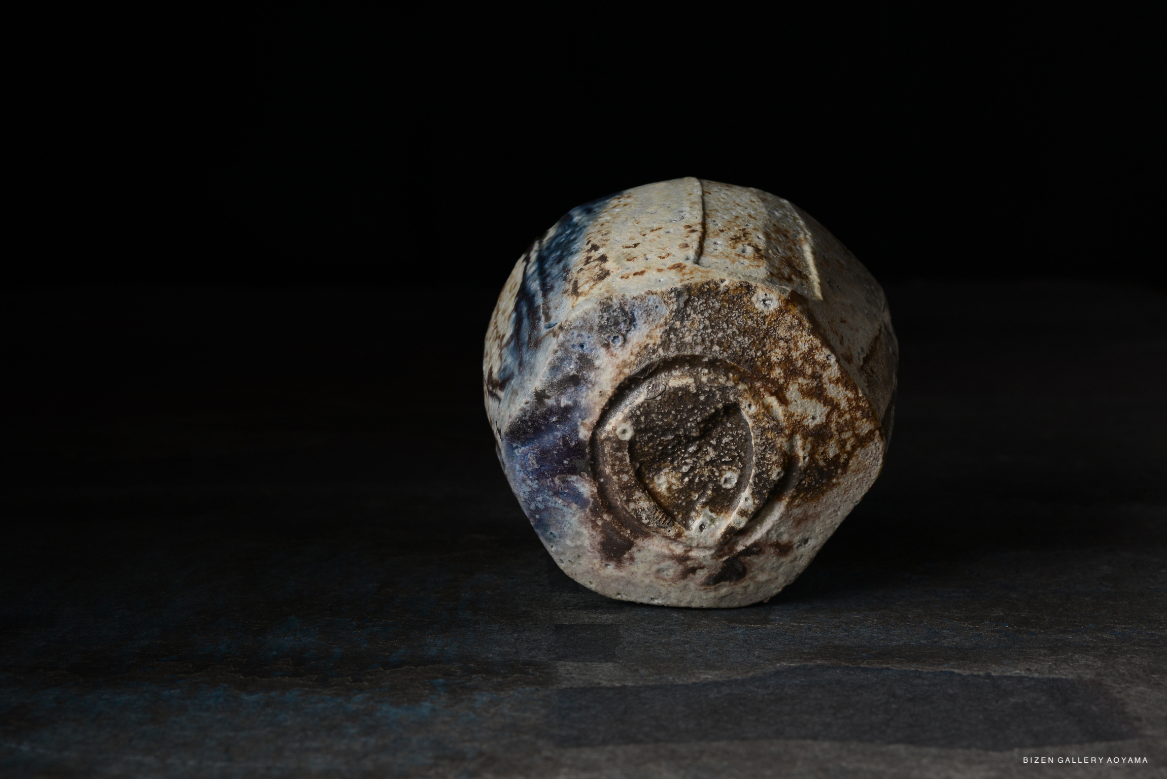 A ceramic pot with a unique, textured surface and a slightly irregular shape, displayed against a dark background.