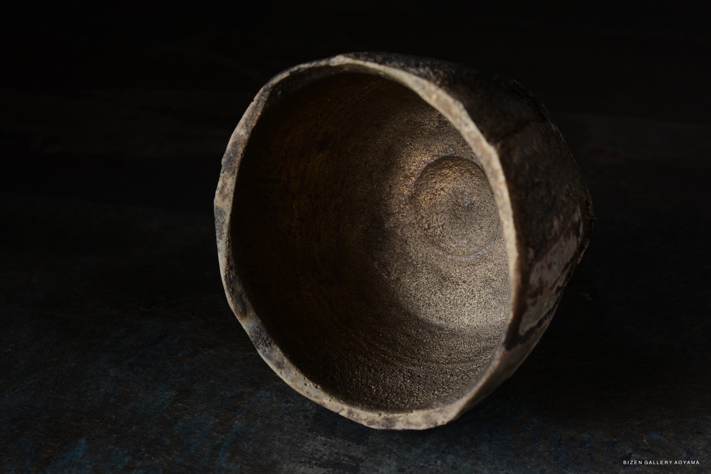 Close-up of the interior of a textured ceramic bowl with rough edges, placed on a dark surface.
