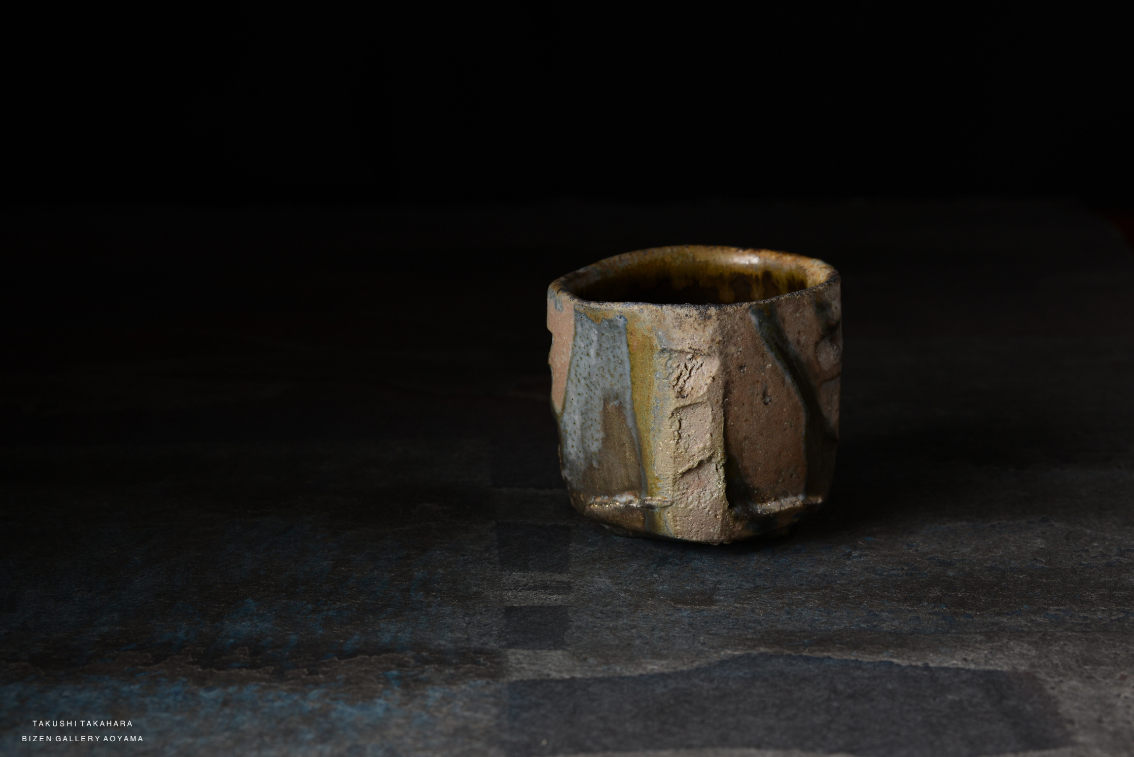A textured ceramic cup with a rustic finish, featuring earthy tones and uneven surfaces, placed on a dark background.