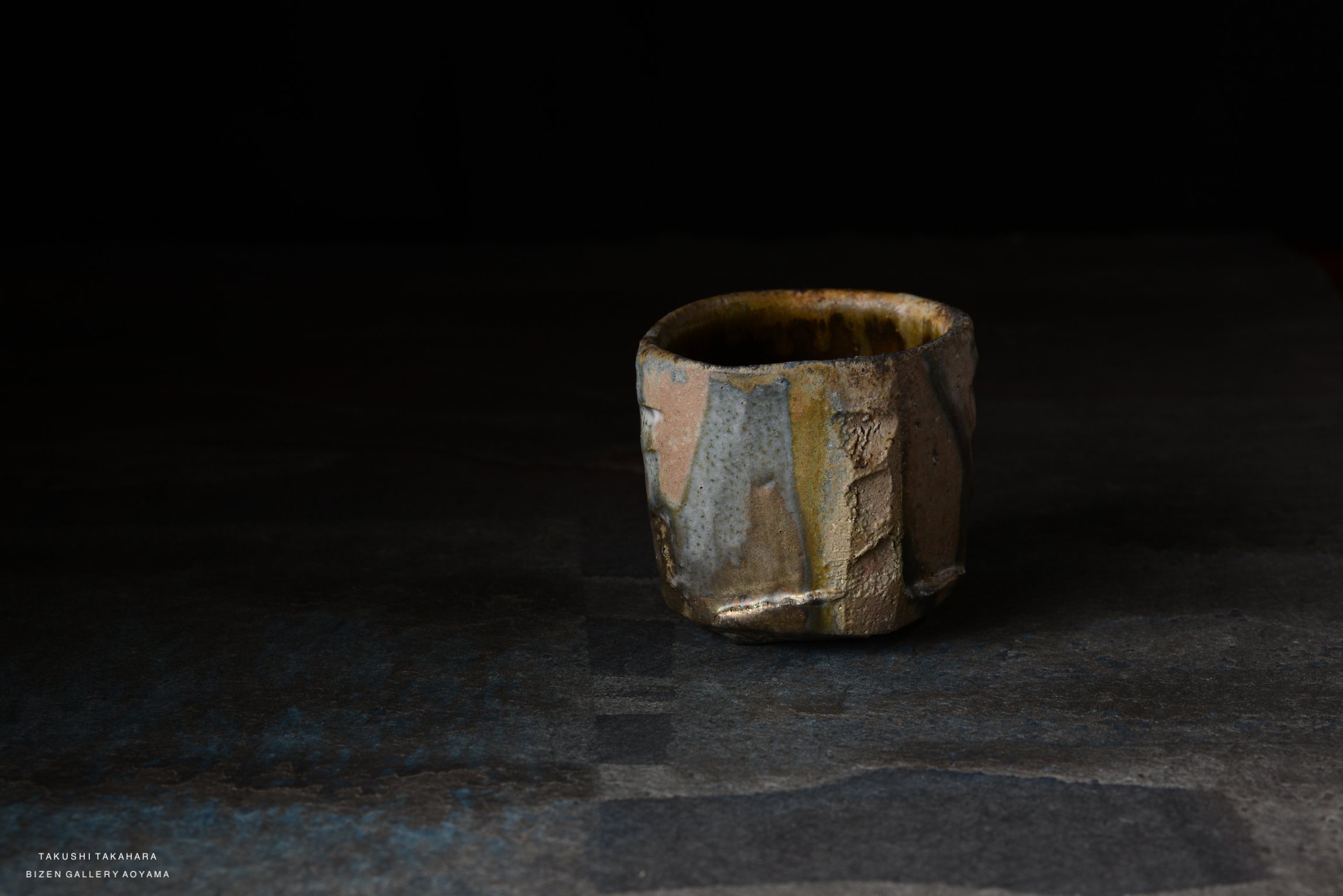 A textured ceramic cup with an irregular shape and earthy tones, positioned on a dark surface.
