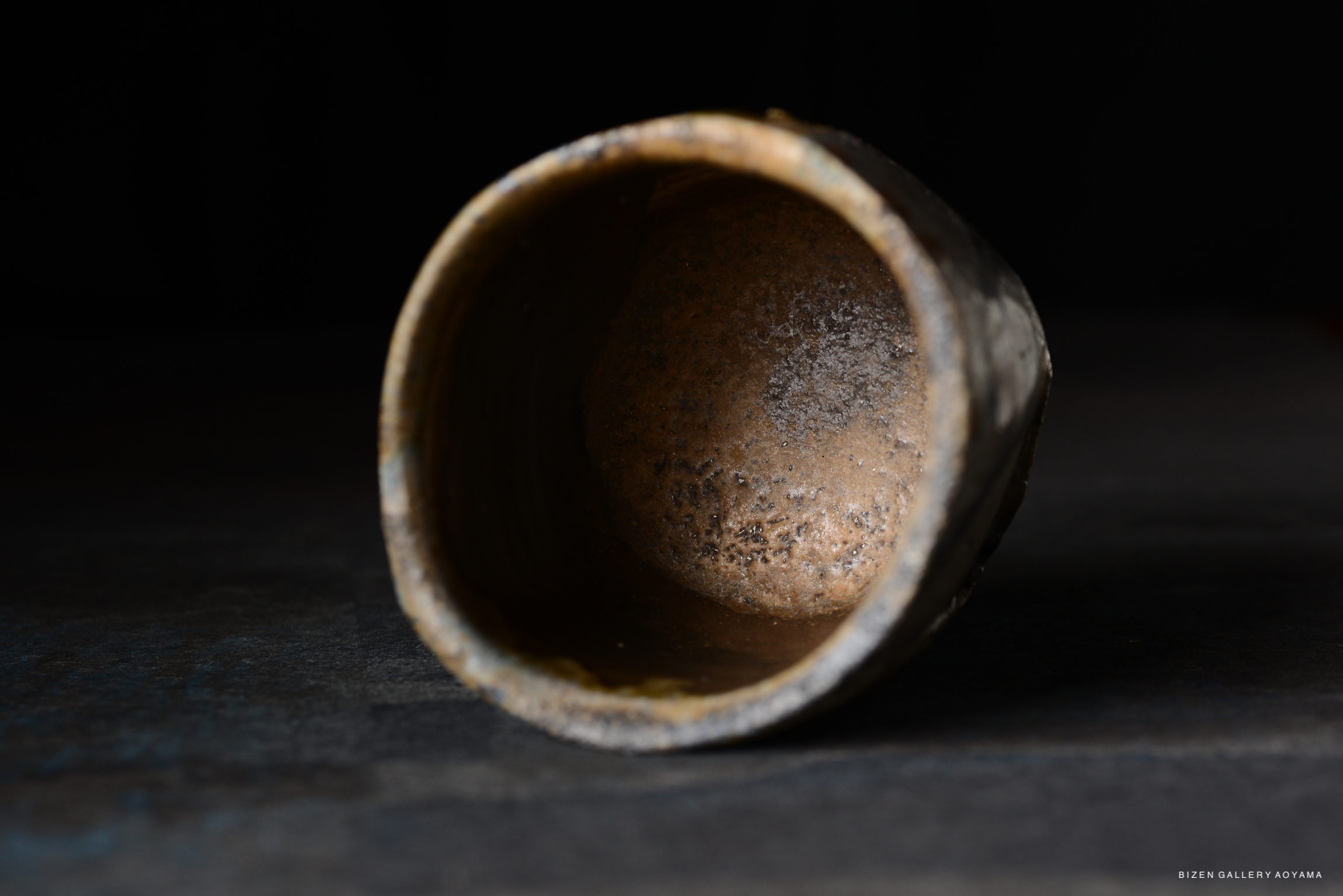 A close-up view of the interior of a rustic pottery cup, showcasing its textured surface and earthy tones against a dark background.