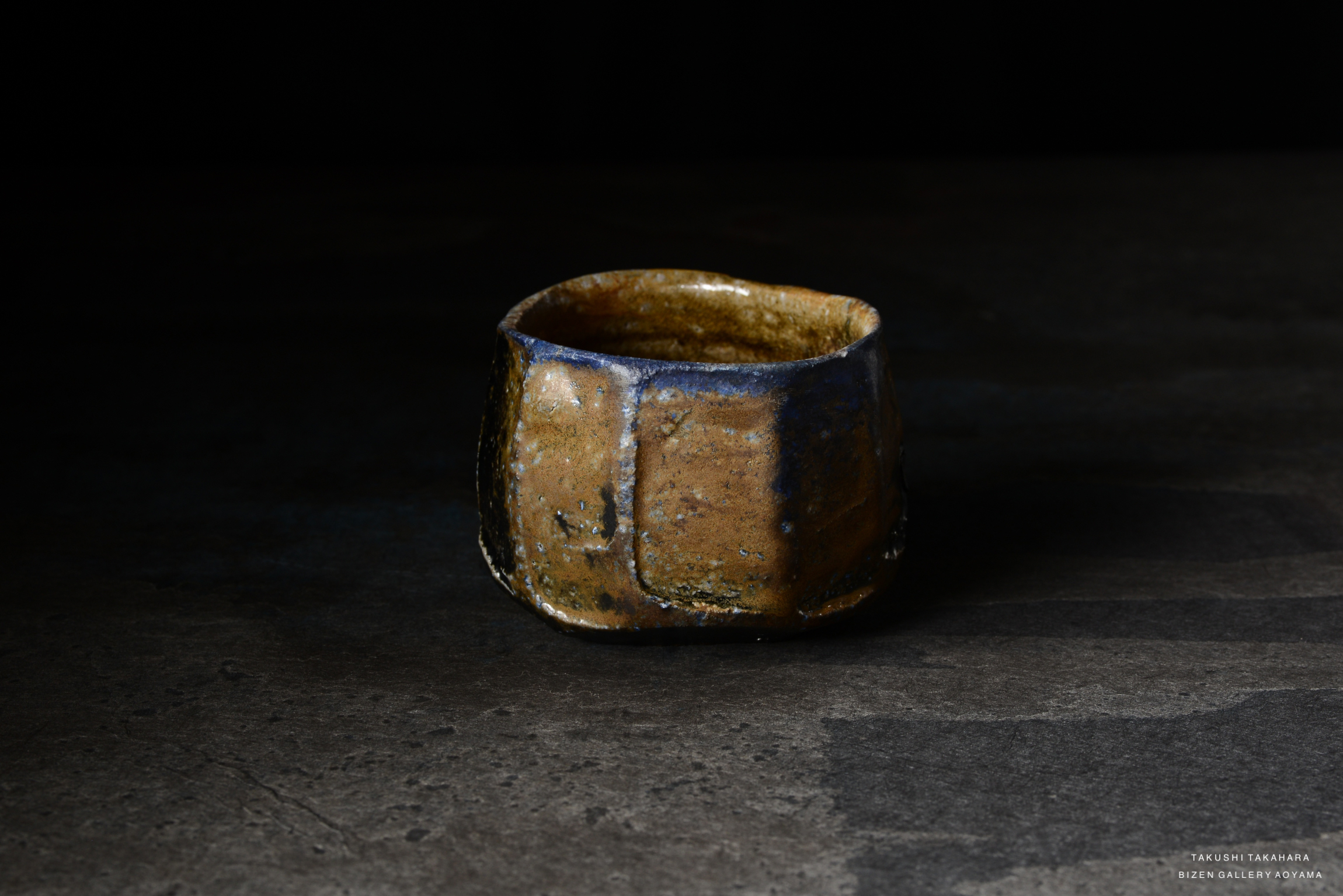A textured ceramic cup with a rustic finish, showcasing earthy tones of brown and blue, set against a dark background.