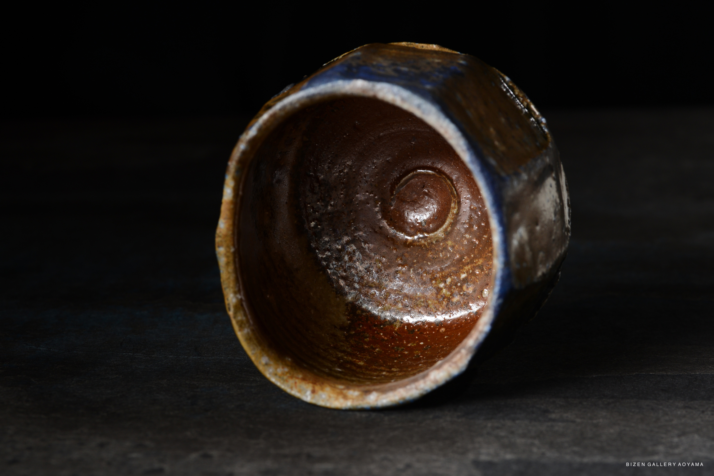 An artistic view of a handcrafted ceramic bowl, showcasing a textured, spiraled interior with a mix of earthy brown and blue glazes.