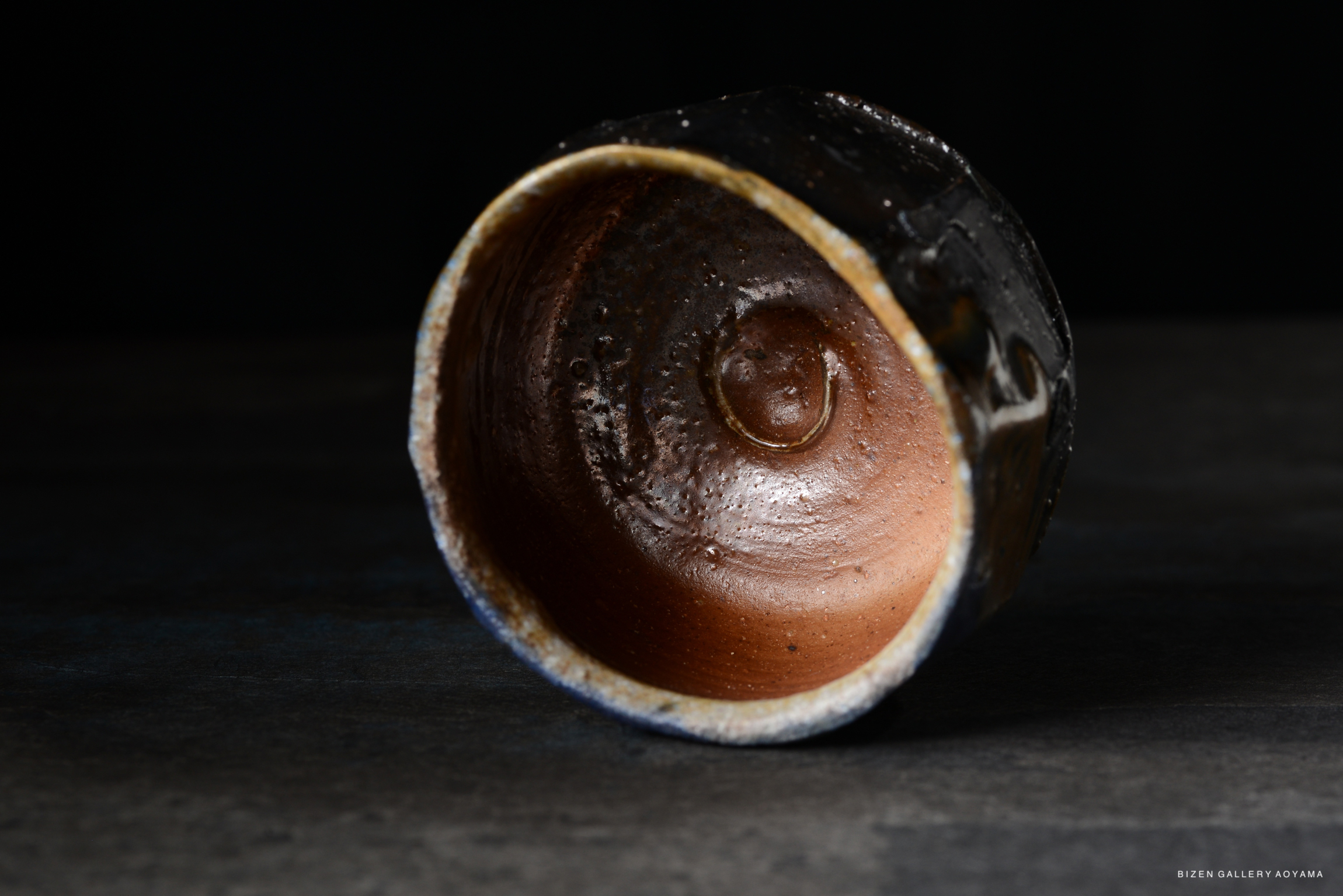 A close-up view of the interior of a rustic clay bowl, showcasing its textured brown and black glaze.