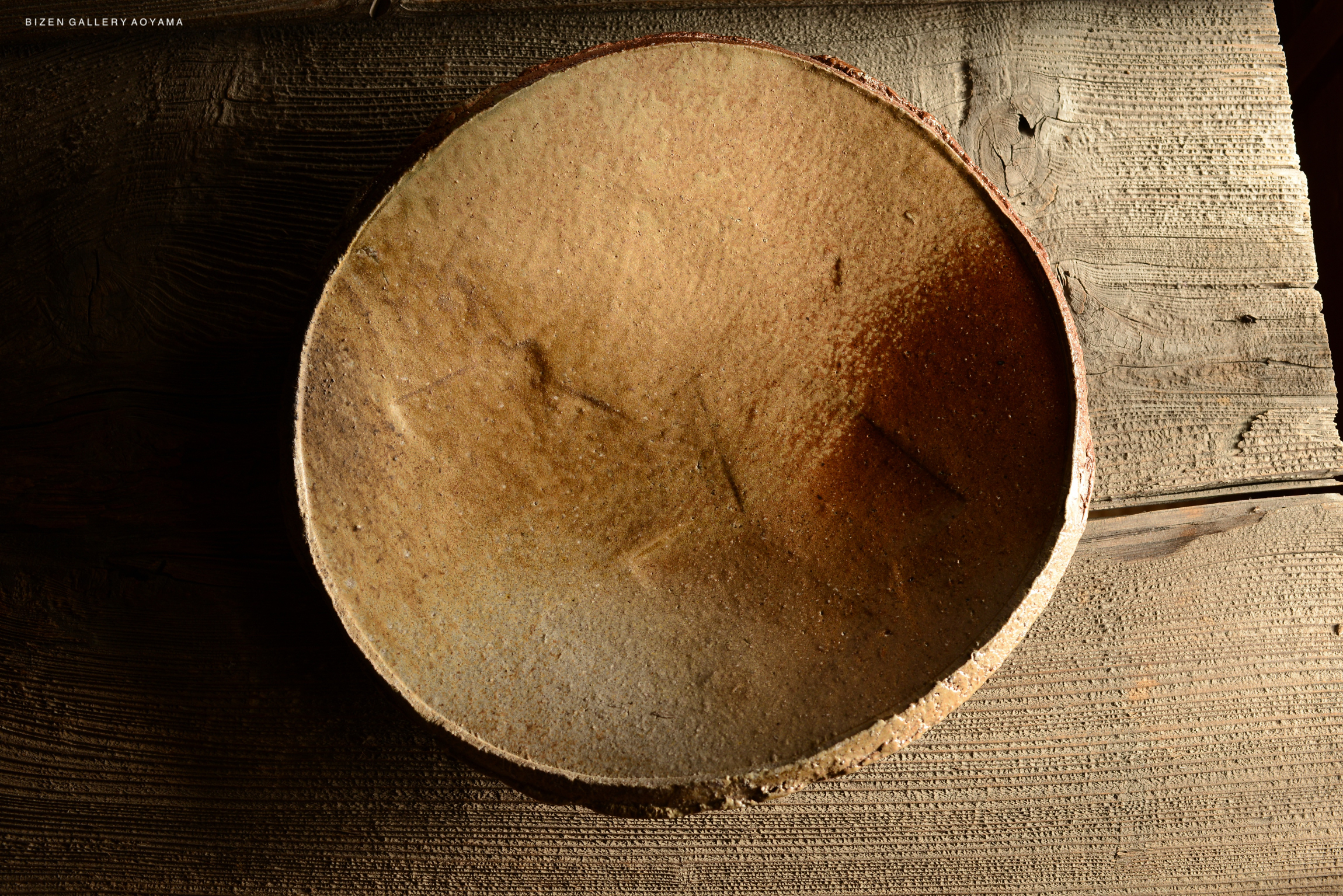 A handcrafted ceramic bowl with a textured surface and earthy tones, resting on a wooden table.