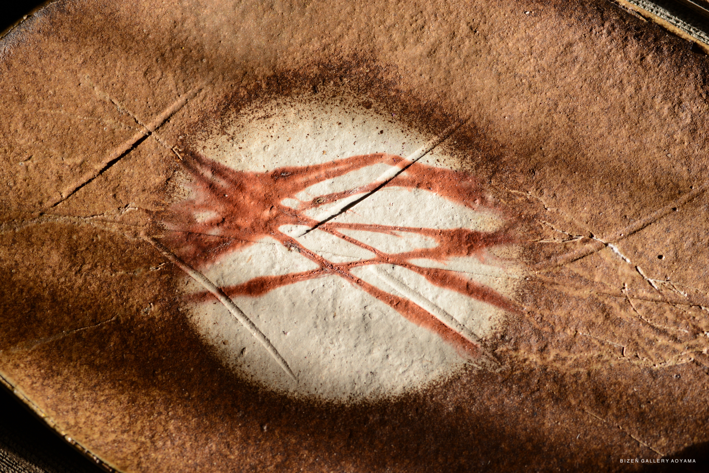 Close-up of a textured ceramic surface featuring abstract patterns of red and brown hues, showcasing artistic markings and natural imperfections.