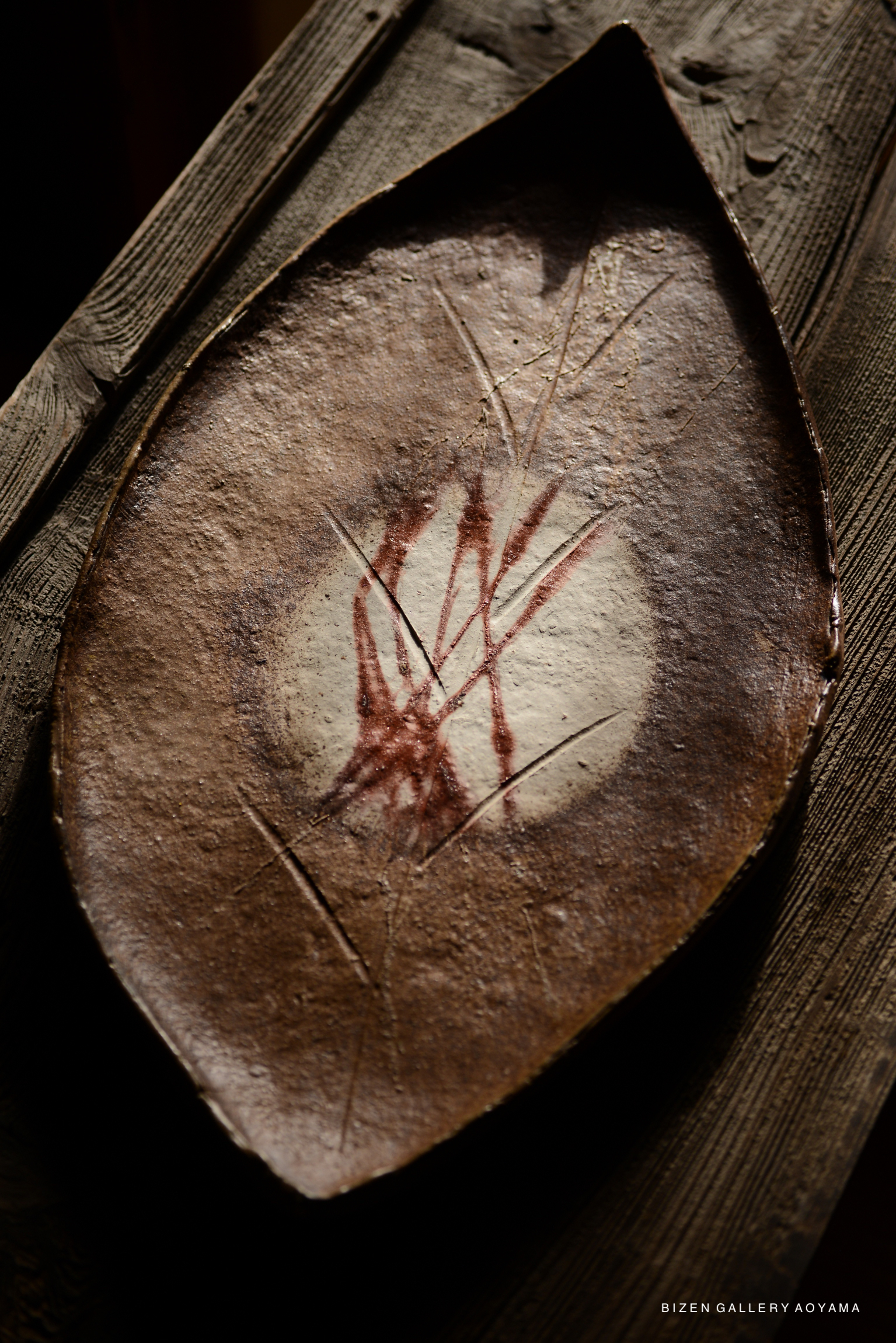 A close-up image of a decorative ceramic plate with a brown surface and red markings, resting on a wooden surface.
